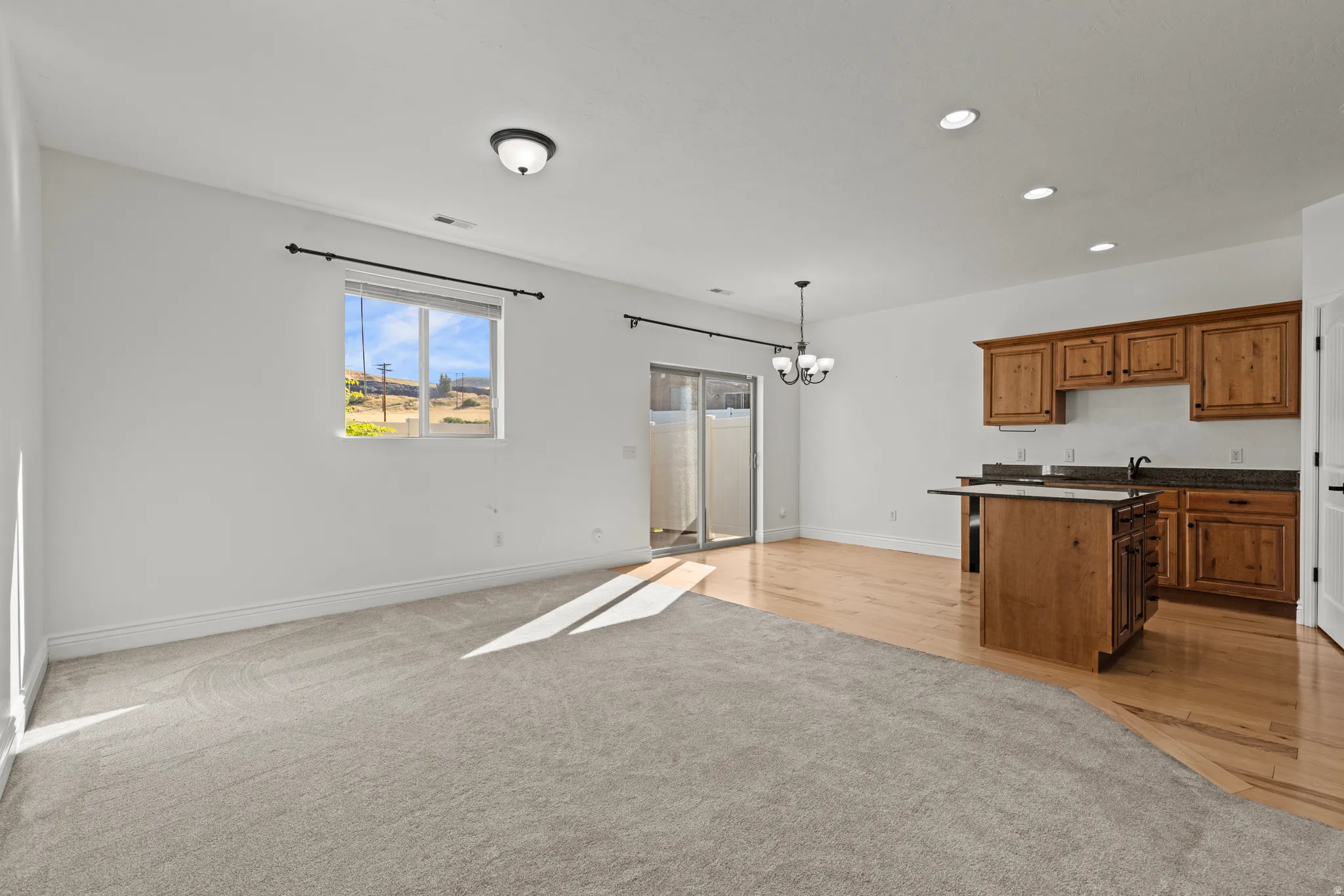 Open-concept room featuring a partial kitchen with wood cabinetry and dark countertops, wood-finish flooring, and a carpeted area