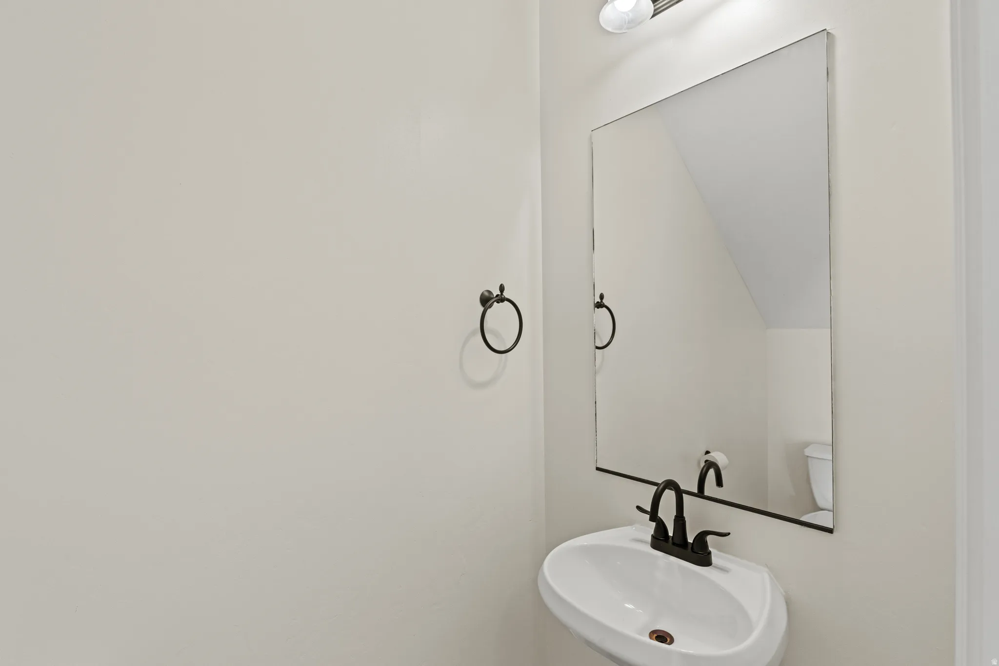Pedestal sink with a matte black faucet, wall-mounted mirror, and an overhead light fixture