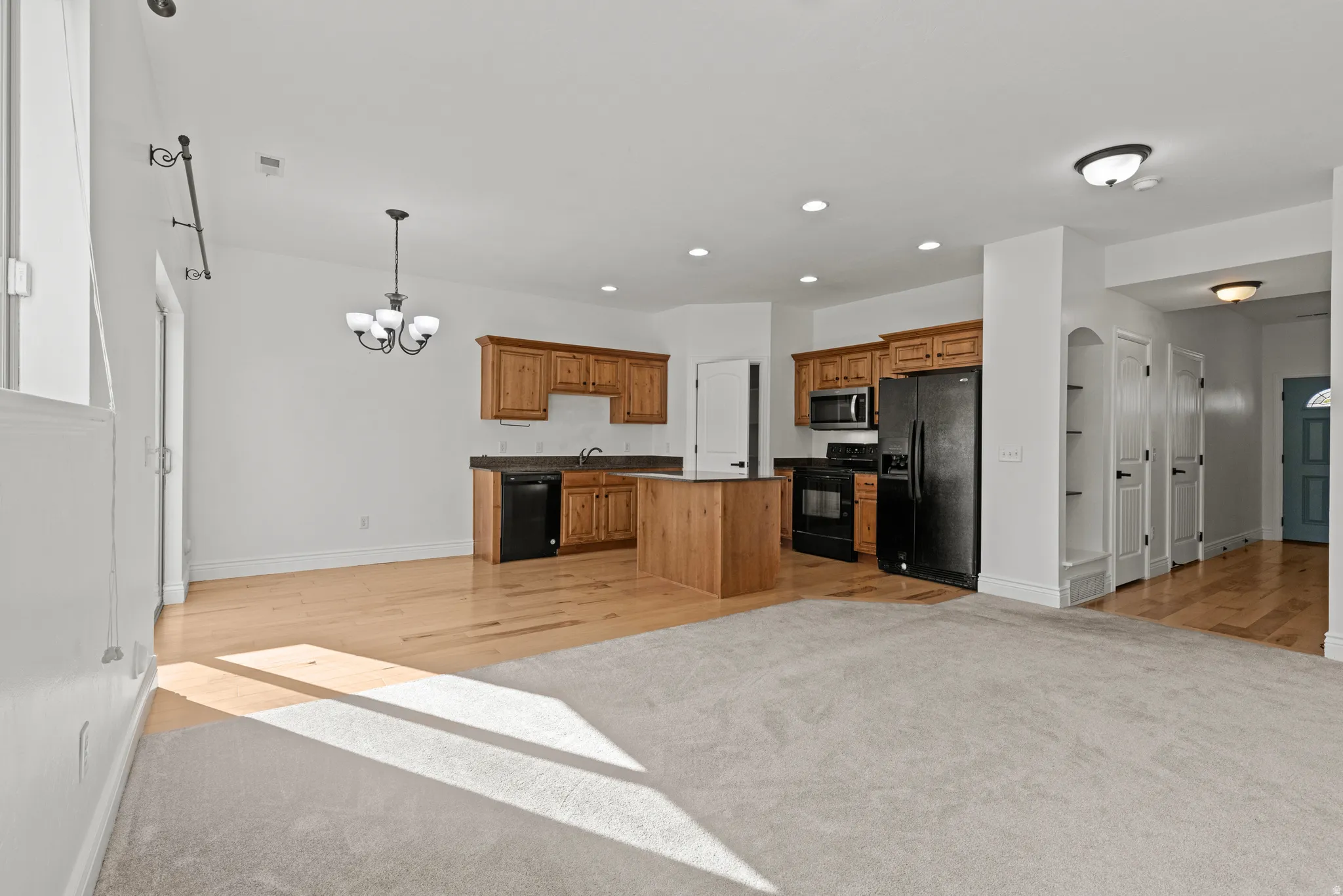 Open-concept living area featuring a kitchen with wood cabinetry, black appliances, and a central island