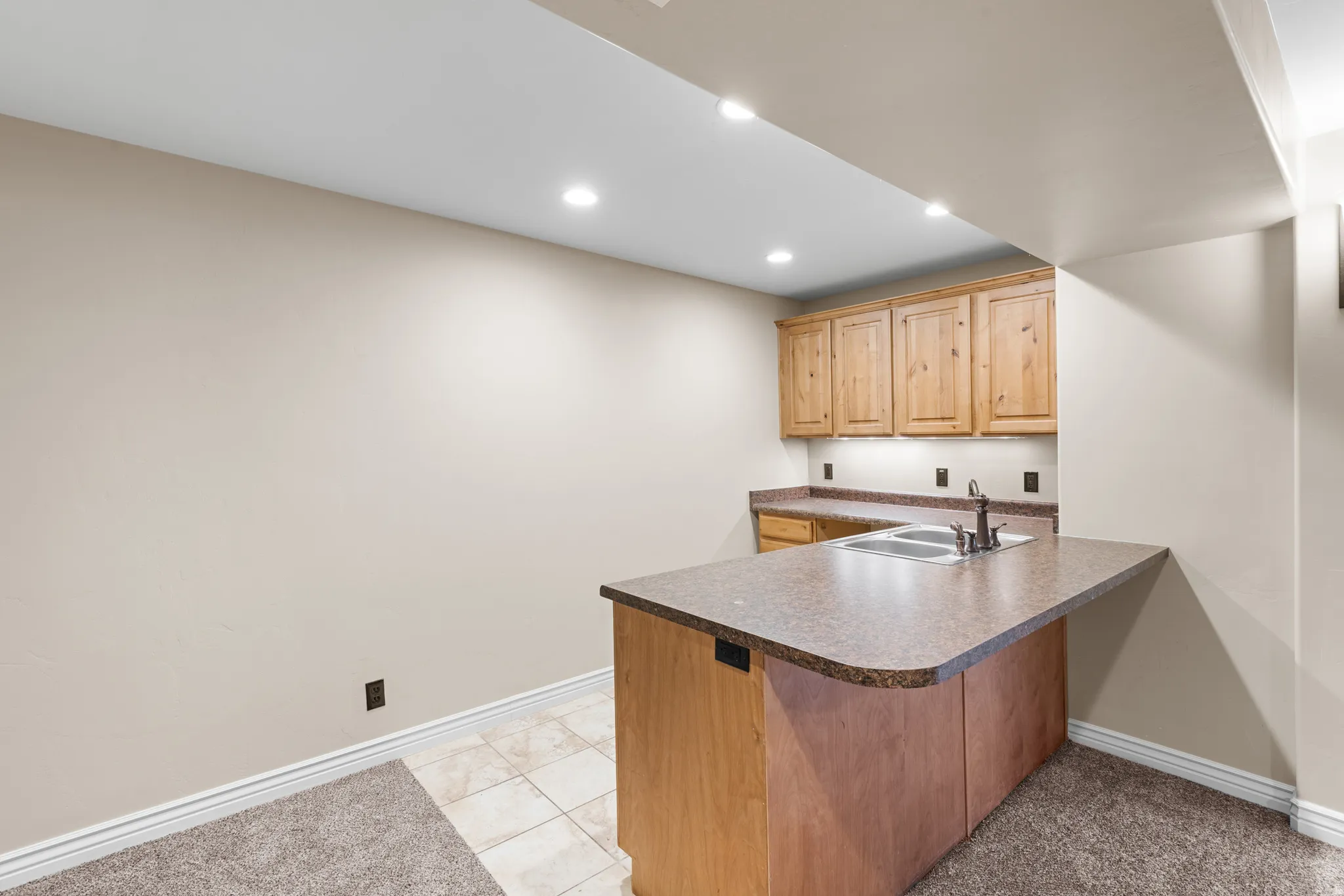 Built-in wet bar featuring a dual basin sink, wood-finish cabinetry, and under-cabinet lighting