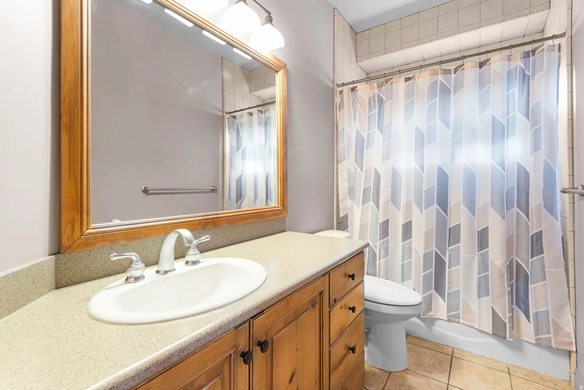 Bathroom vanity featuring a light wood-finish cabinet with multiple drawers and cabinet doors, a light-toned solid surface countertop, and an oval undermount sink with a chrome-finish faucet