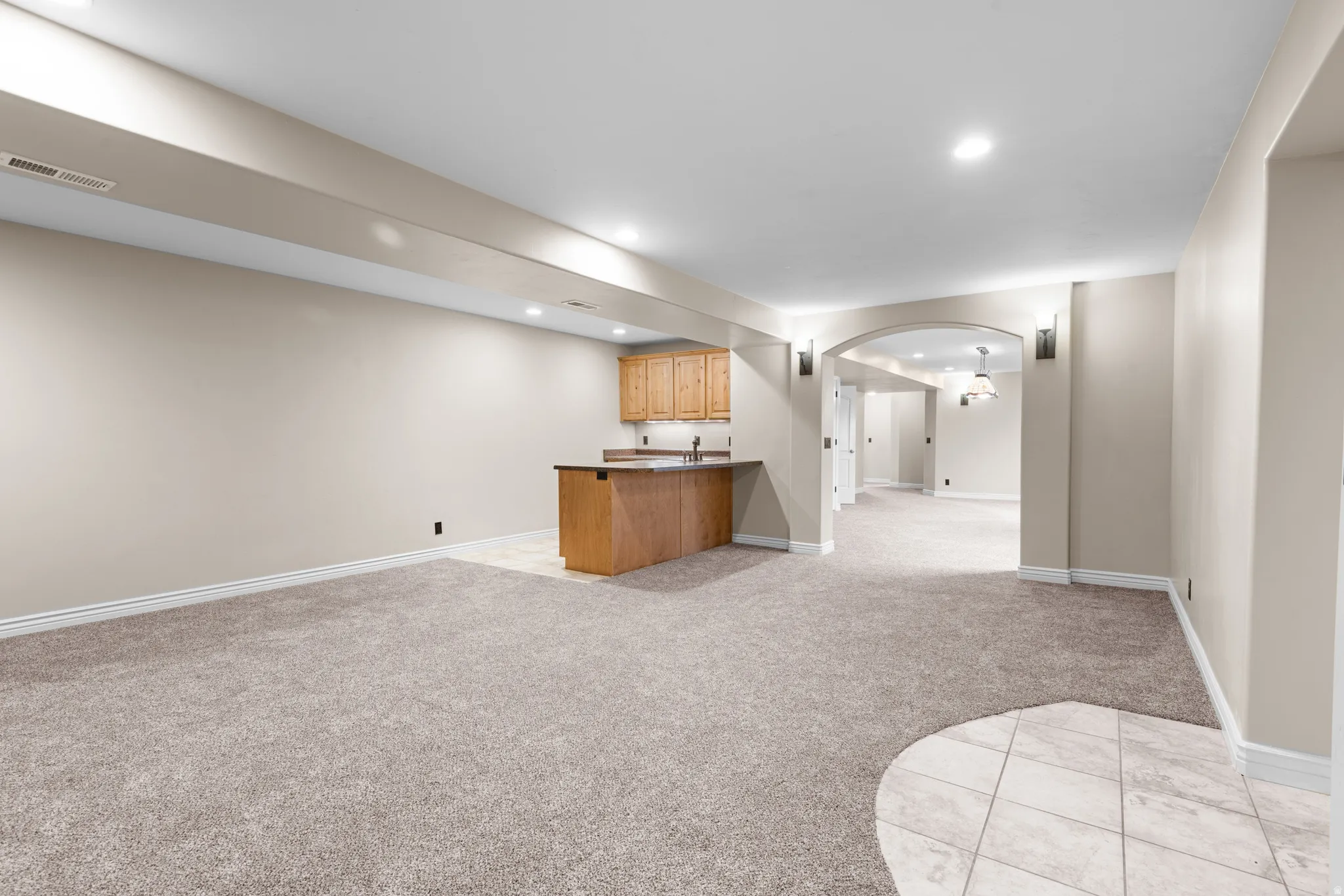 Spacious room featuring neutral carpeting, recessed lighting, a built-in wet bar with wood cabinetry and countertop, and an arched entry