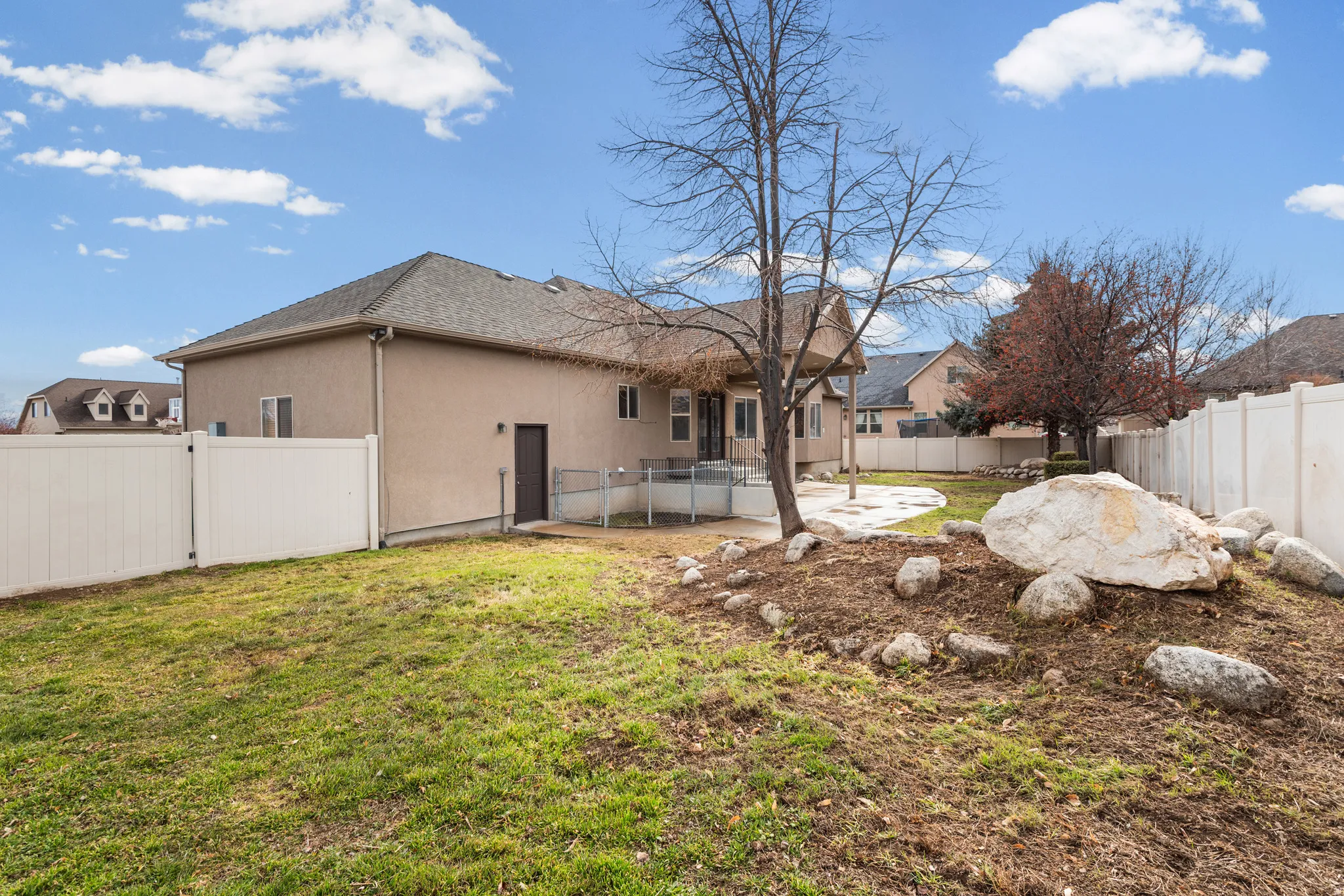 Spacious backyard featuring a sloped lawn, white vinyl fencing, and a stone-accented landscape bed