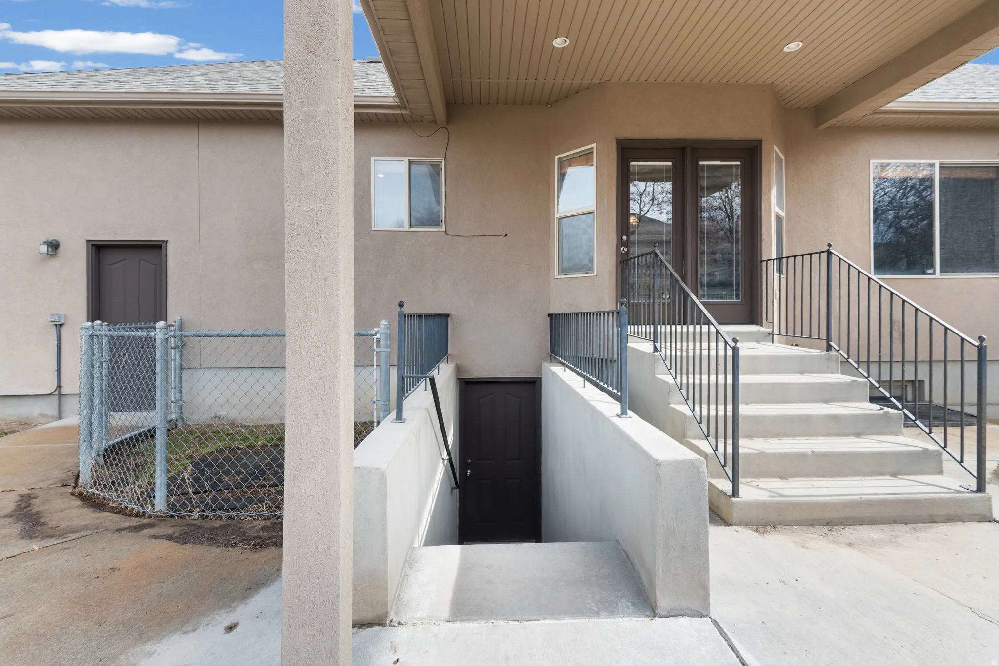 Stucco exterior featuring dual entryways with dark wood-finish doors, concrete steps with black metal railings, and a chain-link fenced area