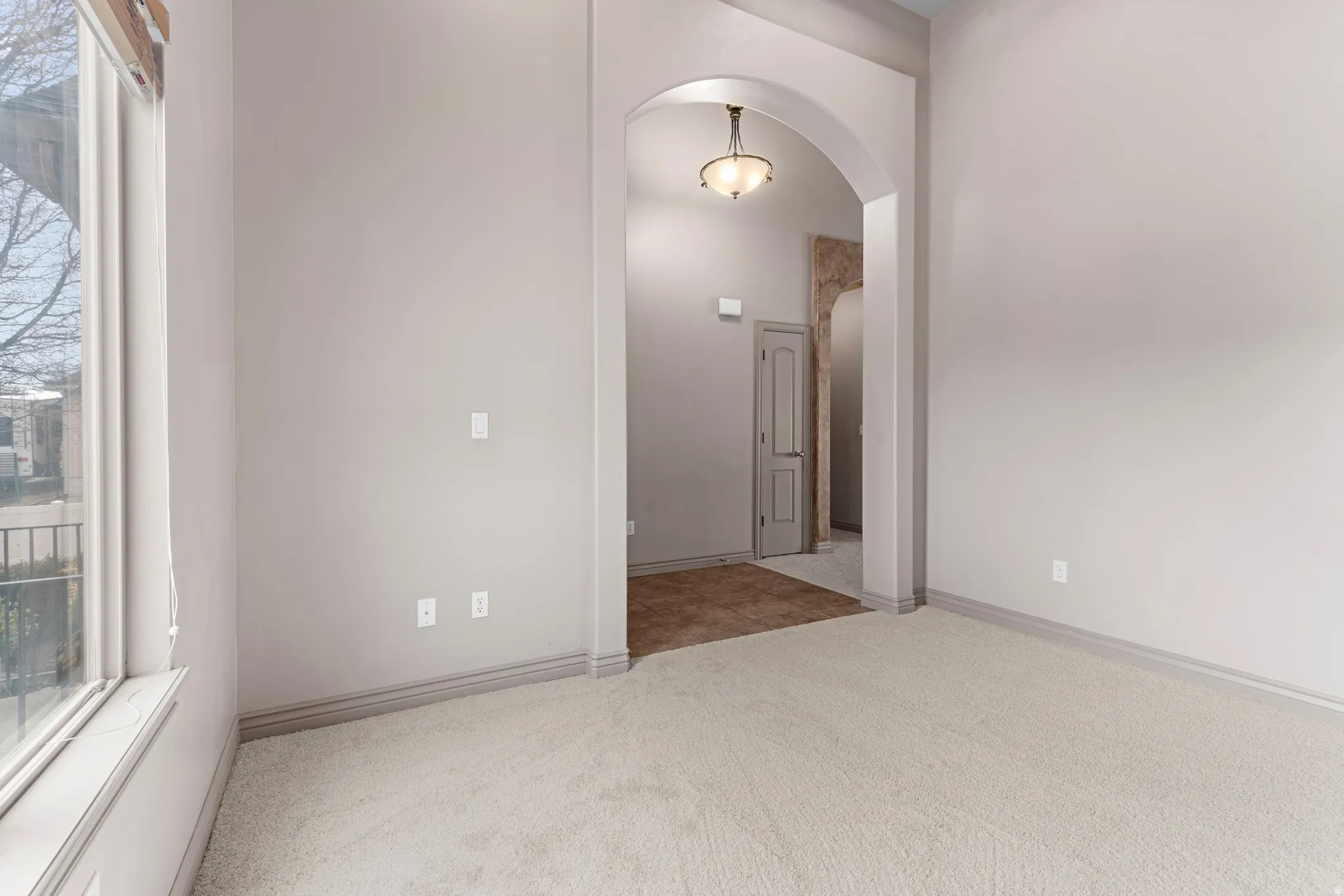 Carpeted room featuring a large window, arched doorway, and neutral wall tones