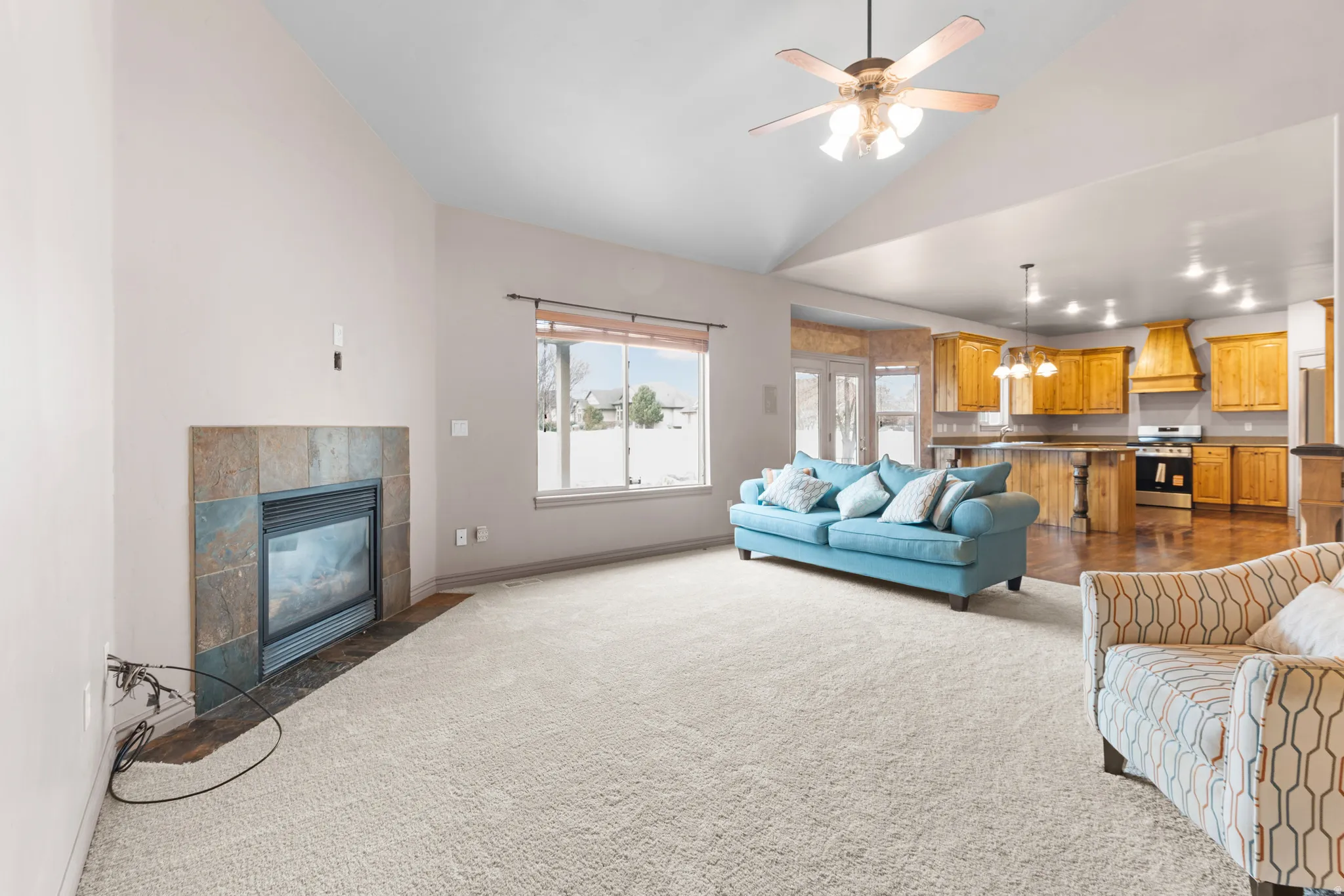 Expansive living area featuring vaulted ceilings, a ceiling fan, and a tiled fireplace