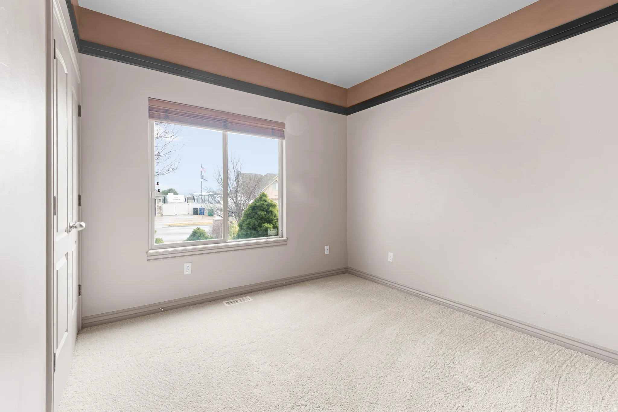 Carpeted room featuring a large window, light-toned walls, and a multi-toned crown molding detail
