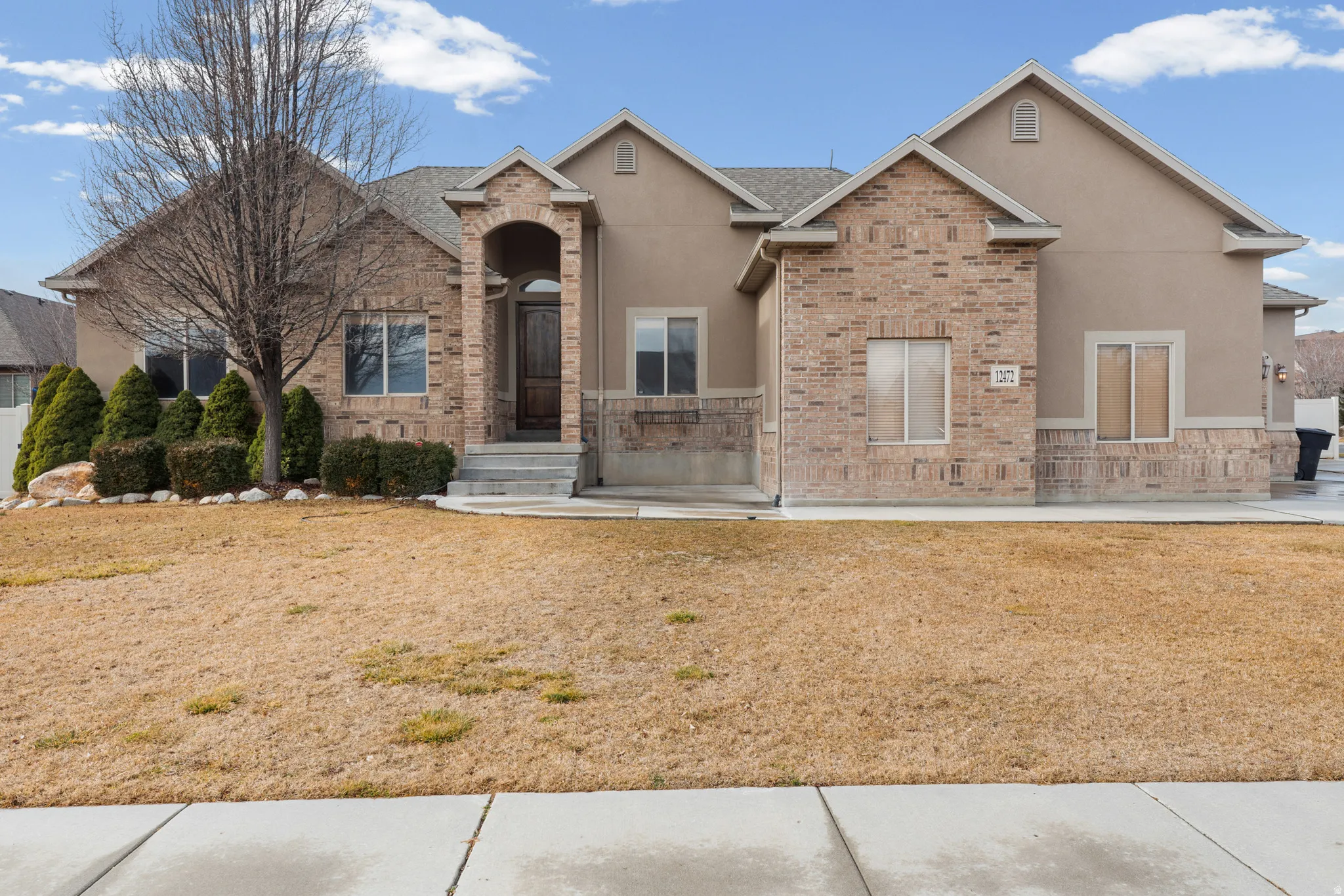 Tan stucco exterior featuring brick accents, an arched entryway, and a dark wood-finish front door