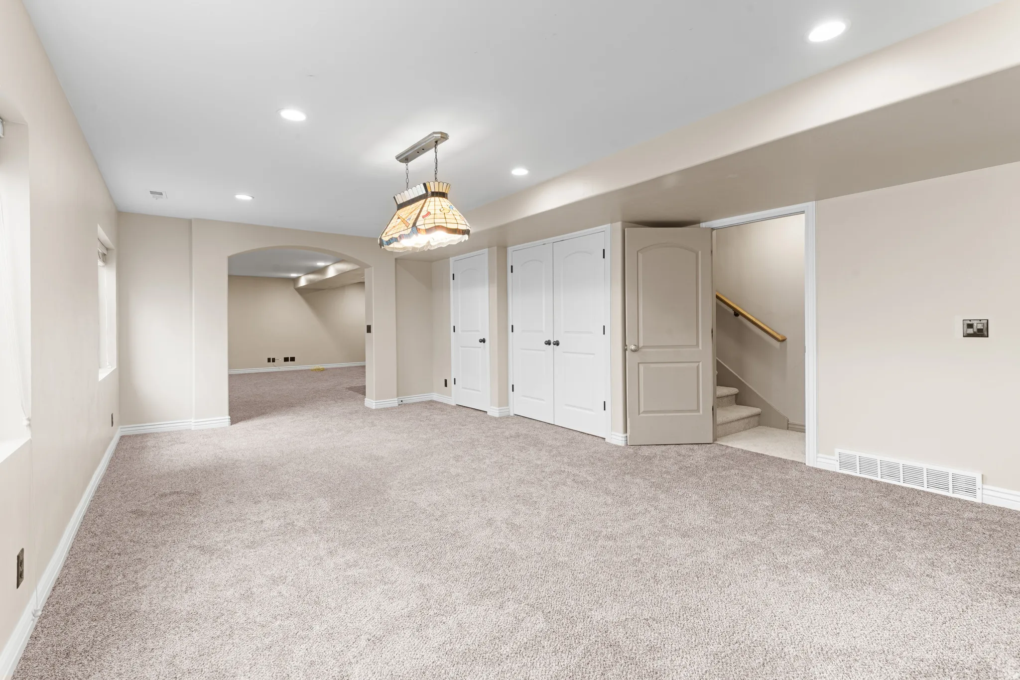 Spacious room with light-toned carpet flooring, recessed lighting, and an arched doorway leading to an additional area