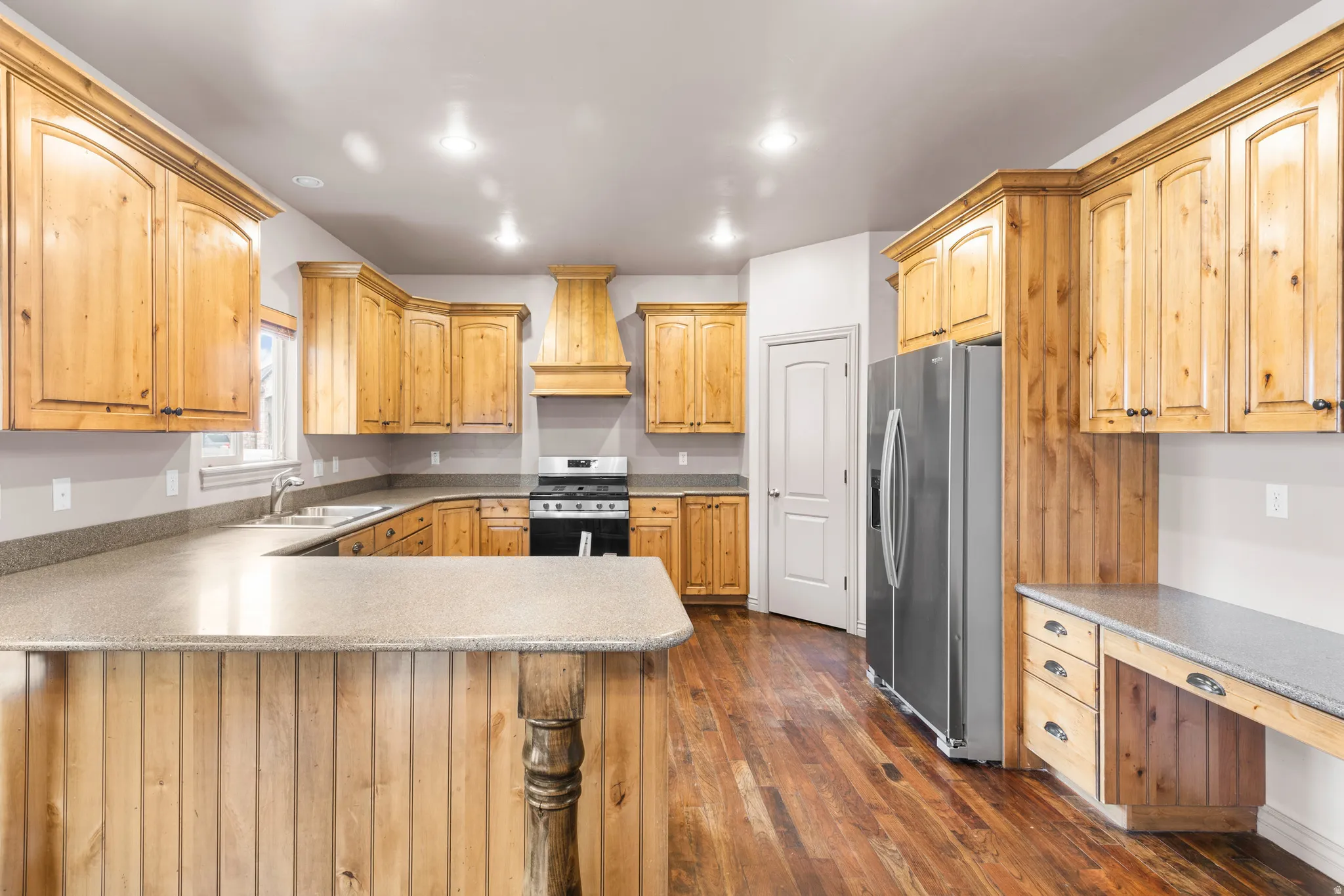 Spacious kitchen featuring extensive natural wood cabinetry, light-toned countertops, stainless steel appliances, and wood-finish flooring