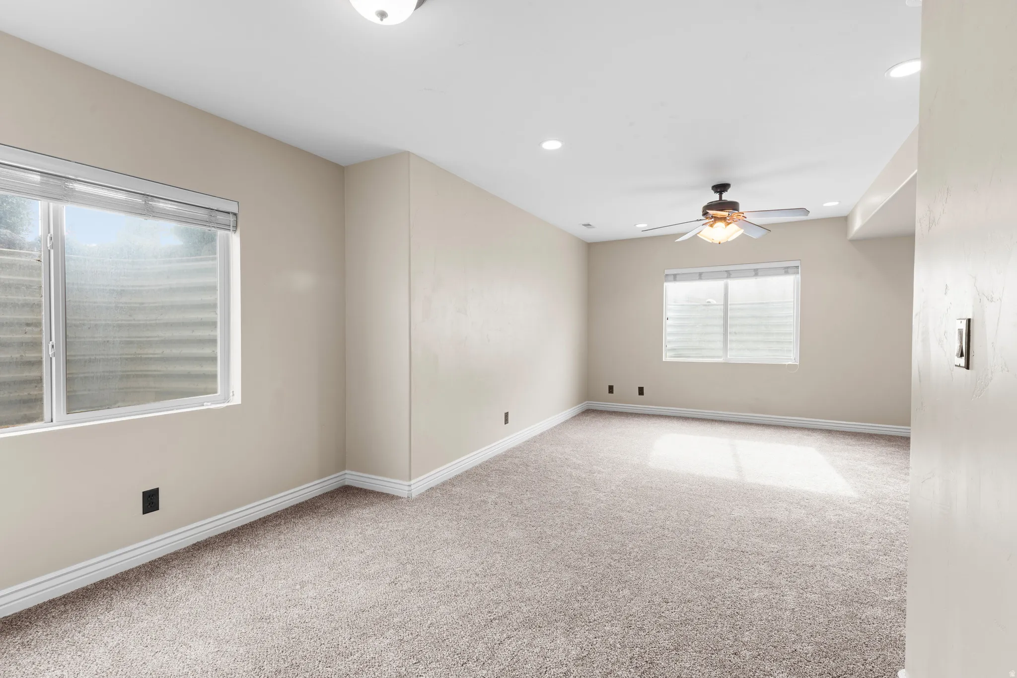 Spacious room featuring neutral carpeting, a ceiling fan, recessed lighting, and two windows with blinds