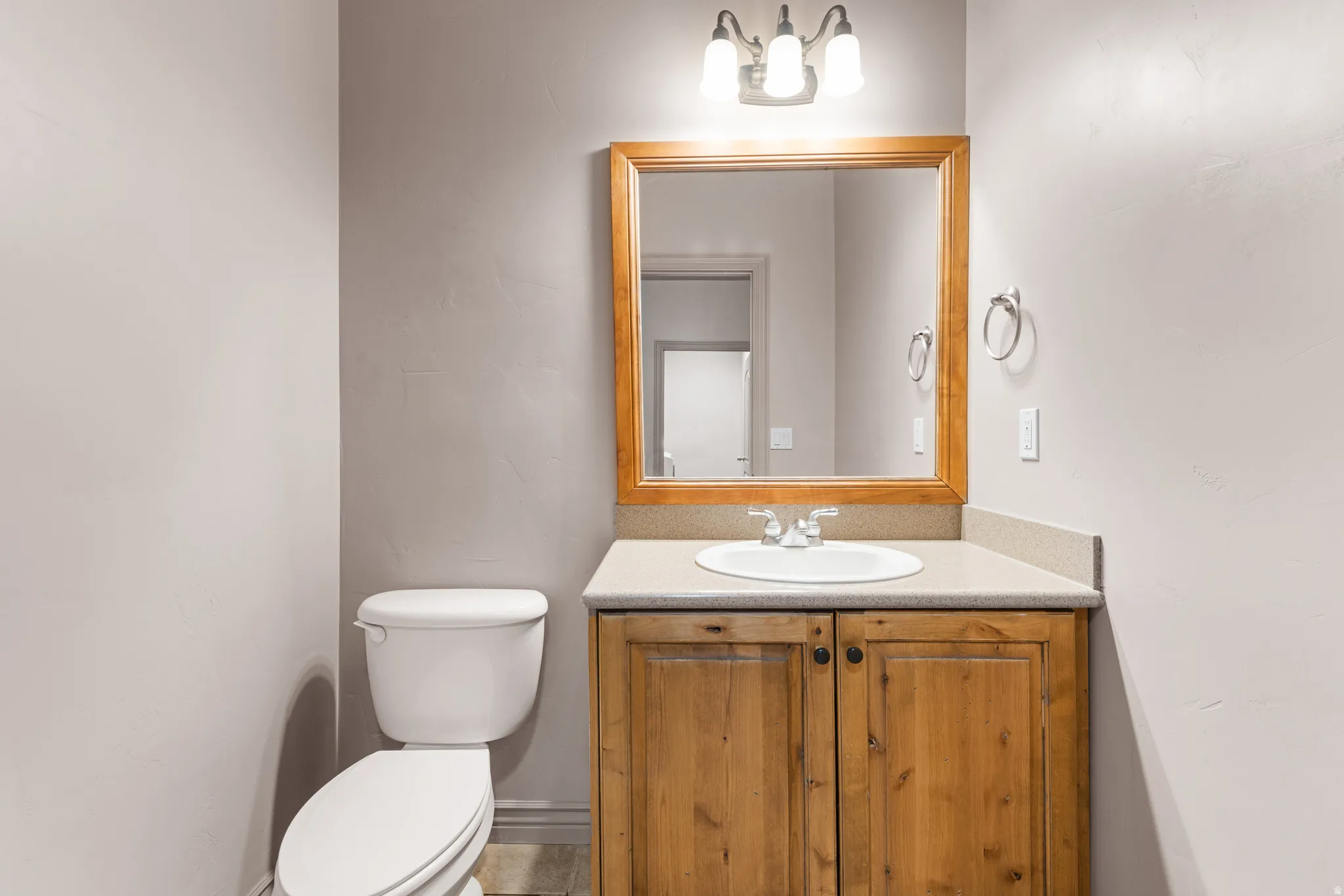 Powder room featuring a single-sink vanity with wood-finish cabinetry, a neutral countertop, and a framed mirror
