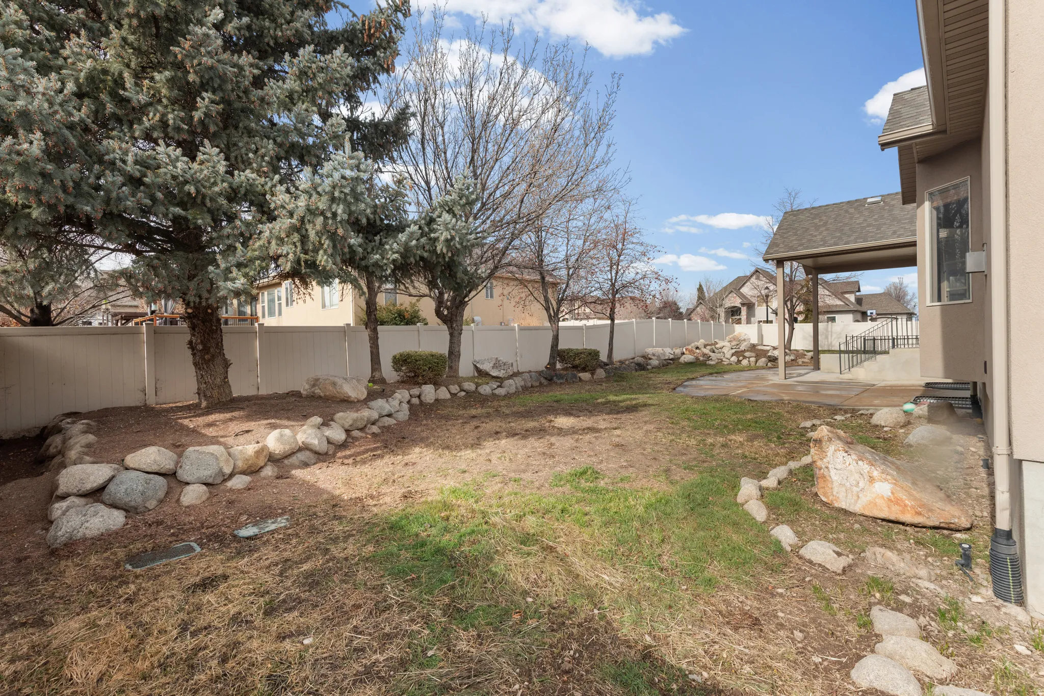 Spacious backyard with a covered patio, rock retaining walls, mature trees, and a privacy fence