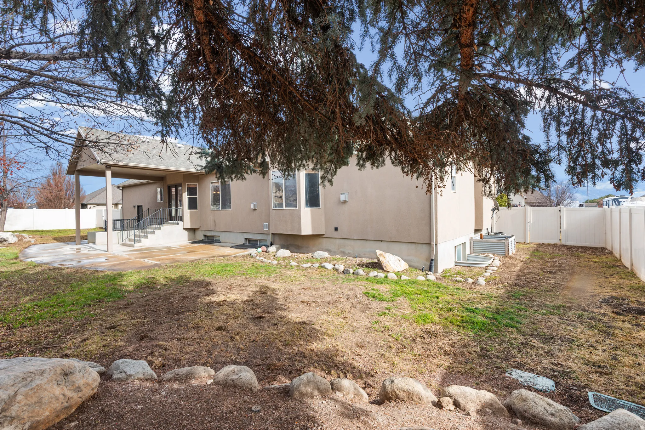 Rear exterior featuring a covered patio, concrete steps with metal railings, a bay window, and a white privacy fence