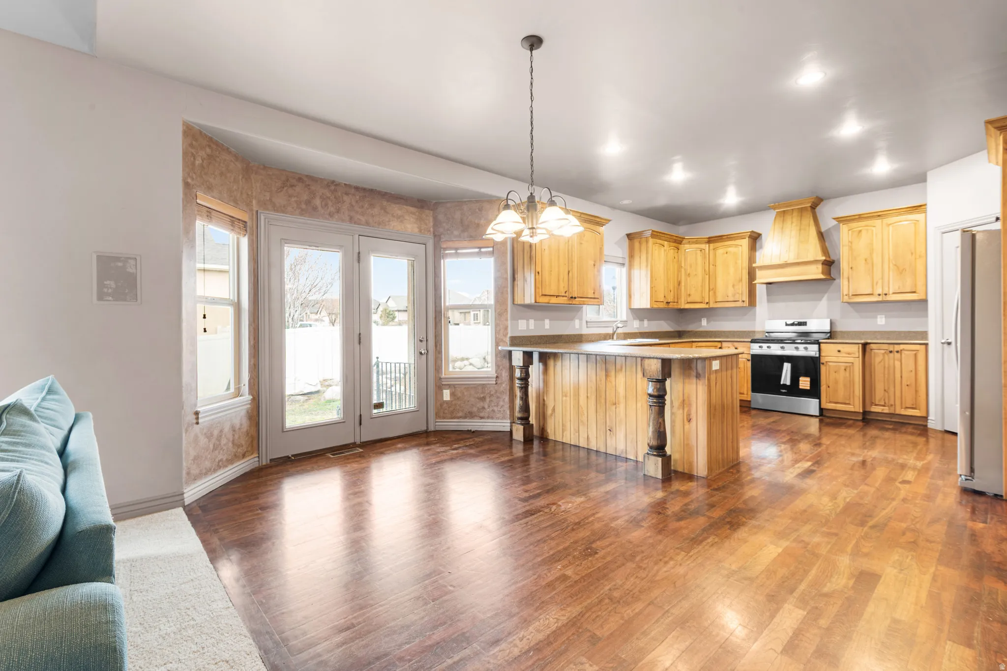 Expansive kitchen and dining area featuring rich wood-finish flooring, light wood cabinetry, and a central island with decorative posts