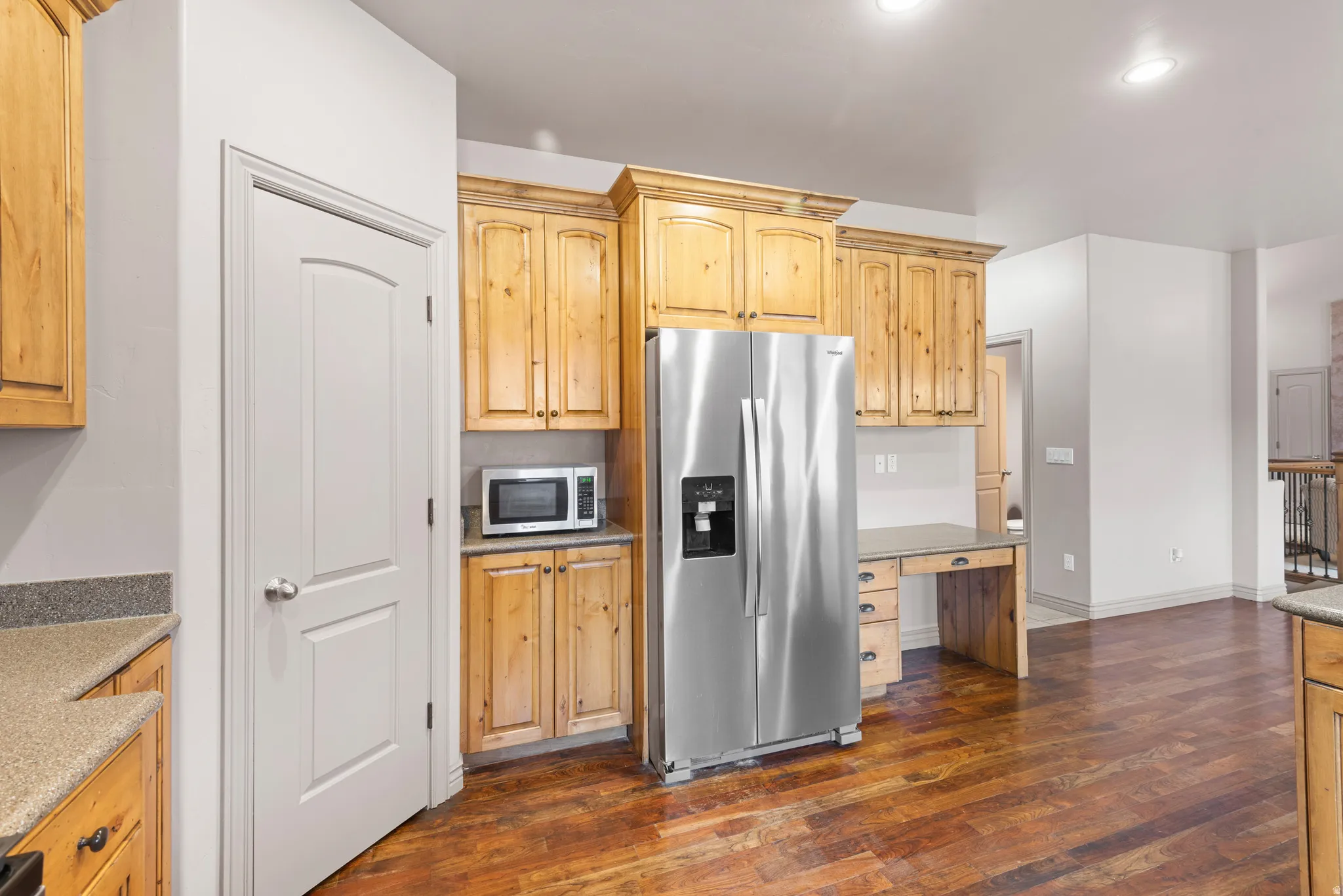 Kitchen area featuring wood-finish flooring, light wood cabinetry, stainless steel refrigerator, and a built-in desk area with drawers