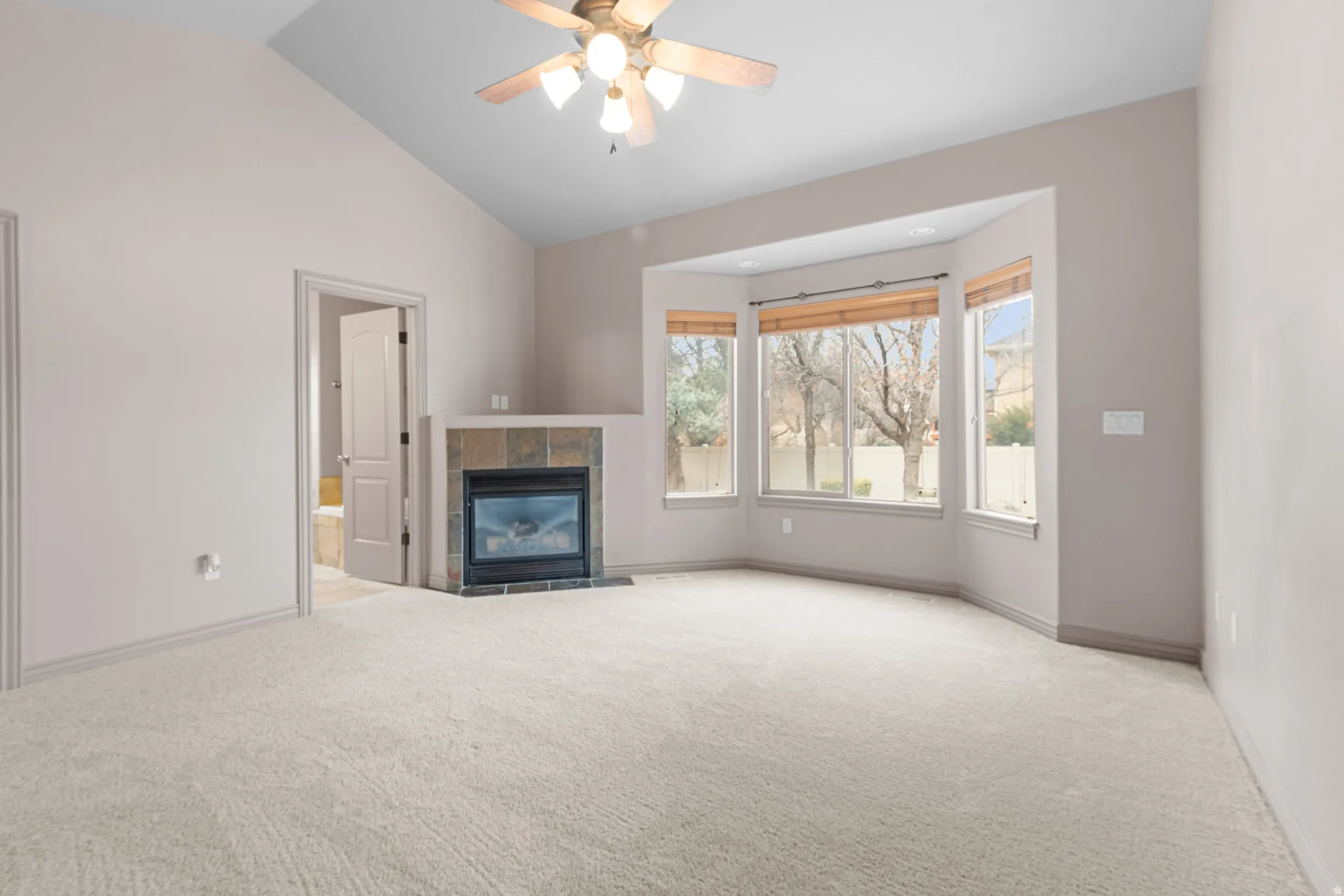 Spacious room featuring vaulted ceilings, a ceiling fan with integrated lighting, and carpet flooring