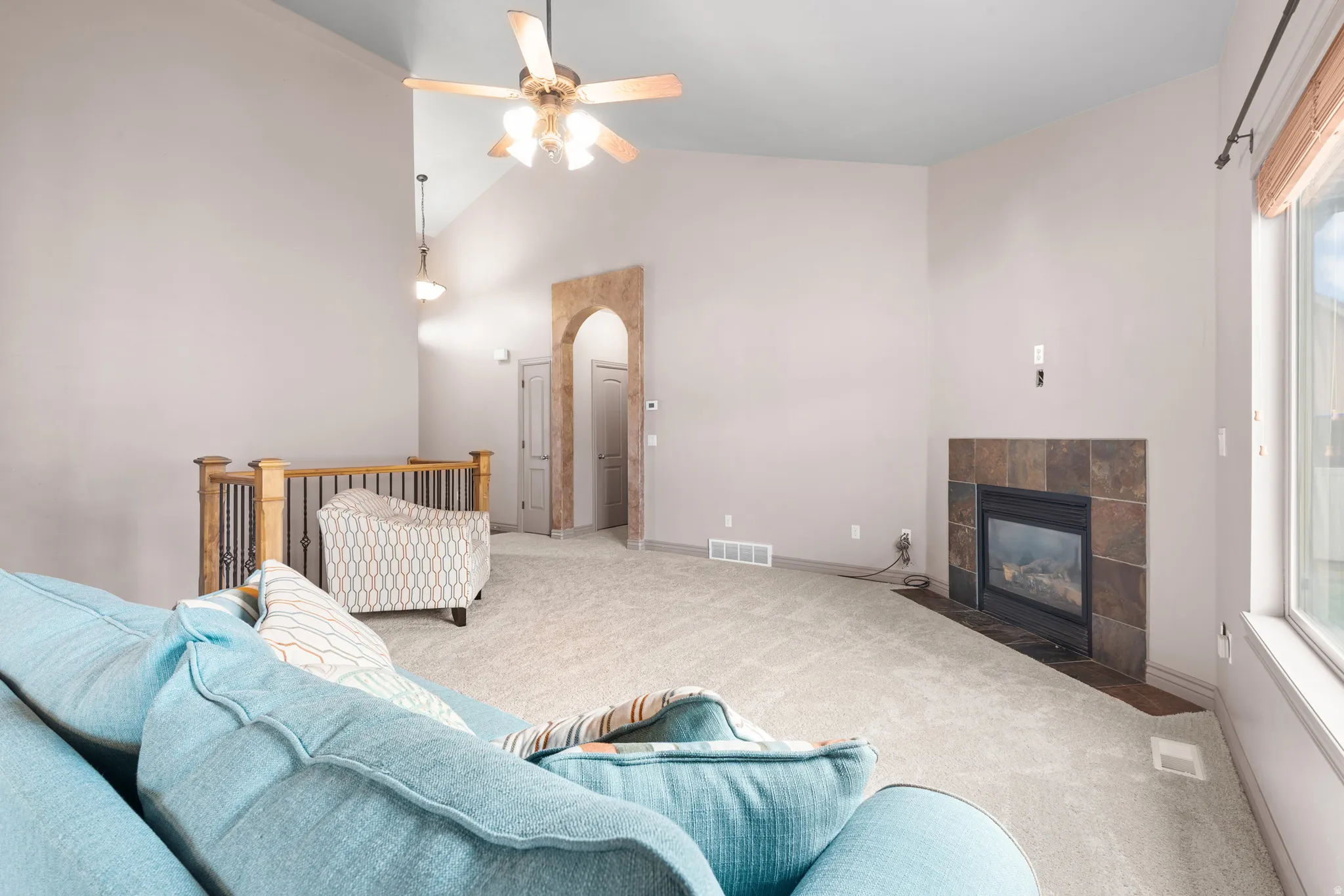 Spacious living area featuring a vaulted ceiling with a ceiling fan, a tiled fireplace, and an arched entry