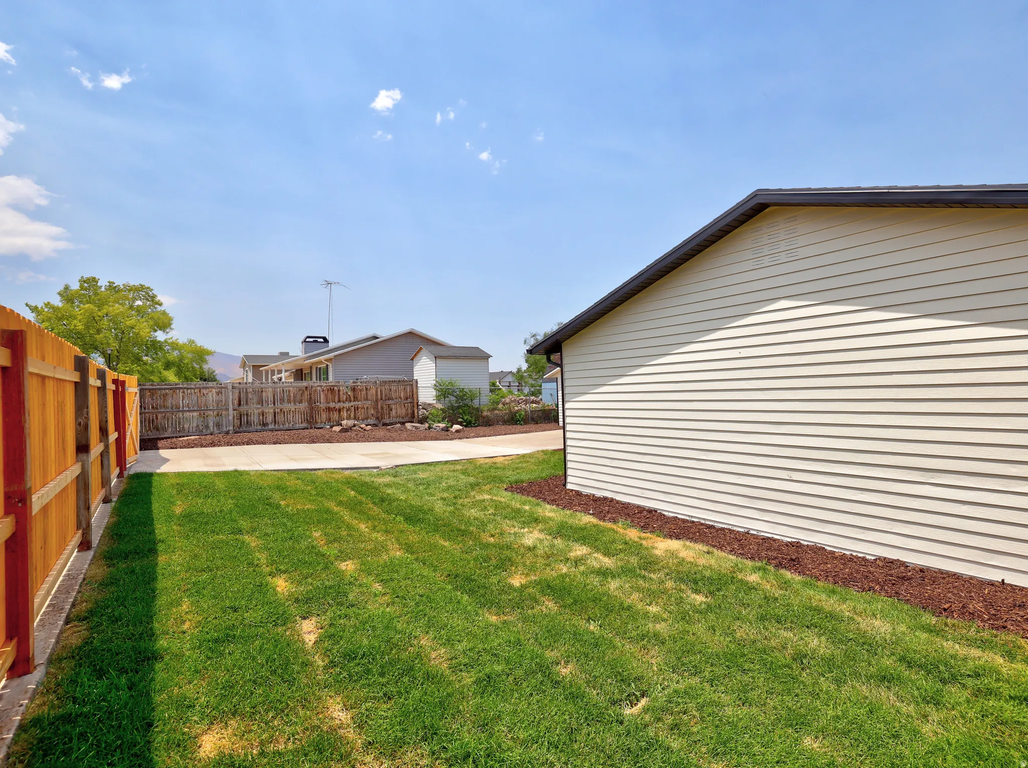Expansive side yard featuring a manicured lawn, a concrete pathway, and a tall wood privacy fence