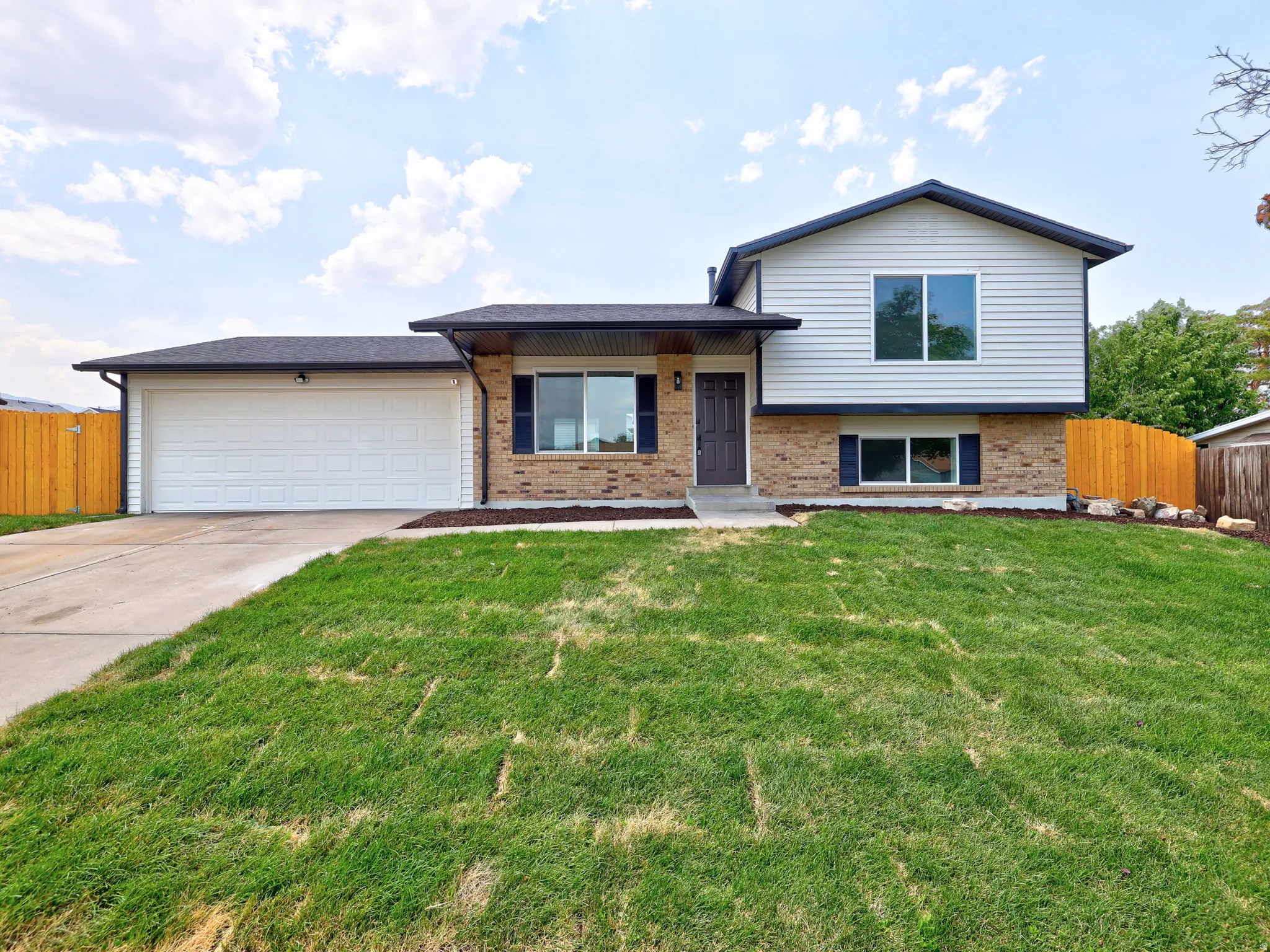 Split-level residence featuring a brick and siding exterior, an attached two-car garage, and a newly installed privacy fence