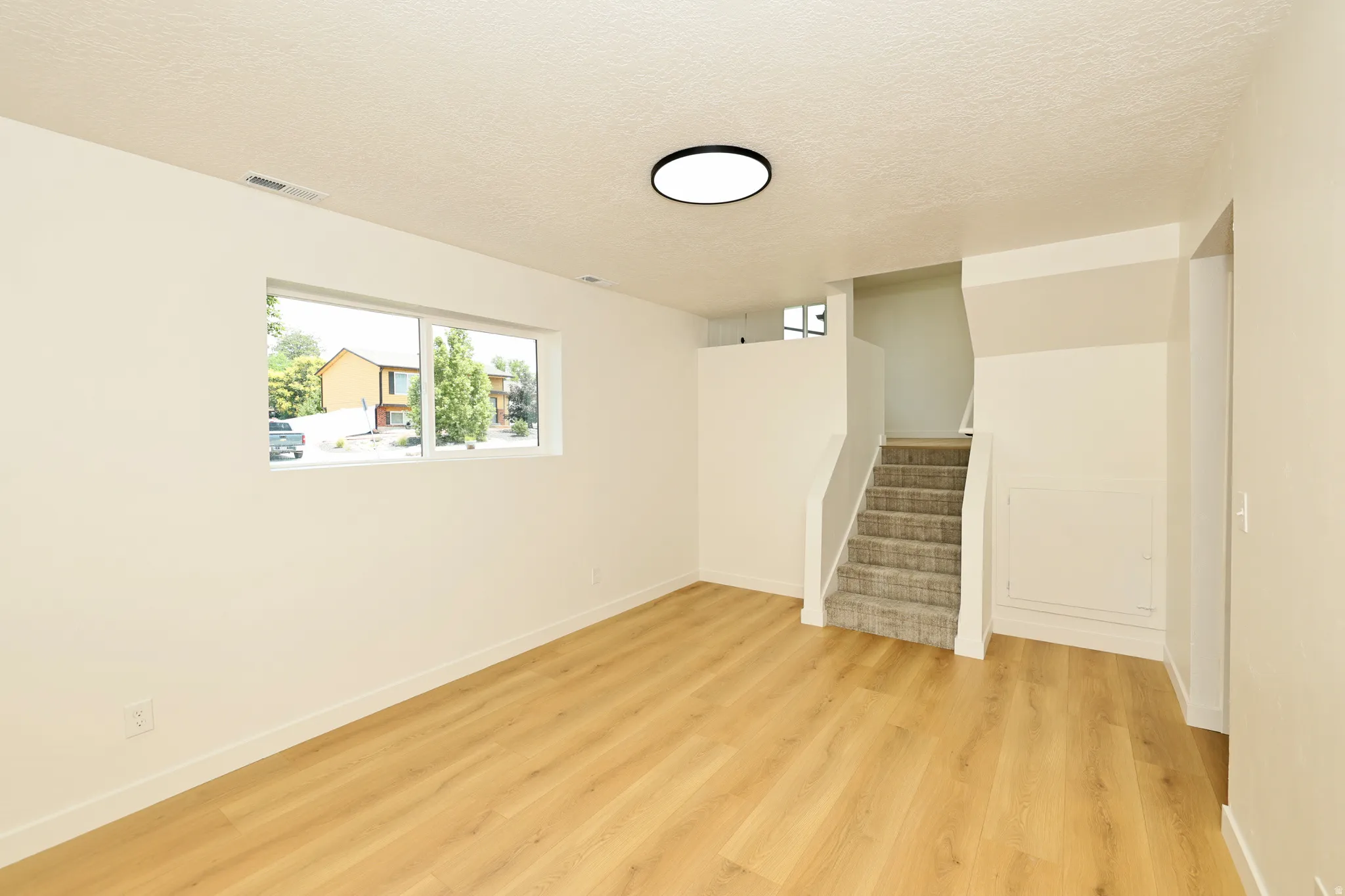 Spacious room featuring wood-finish flooring, light neutral wall paint, and a large window