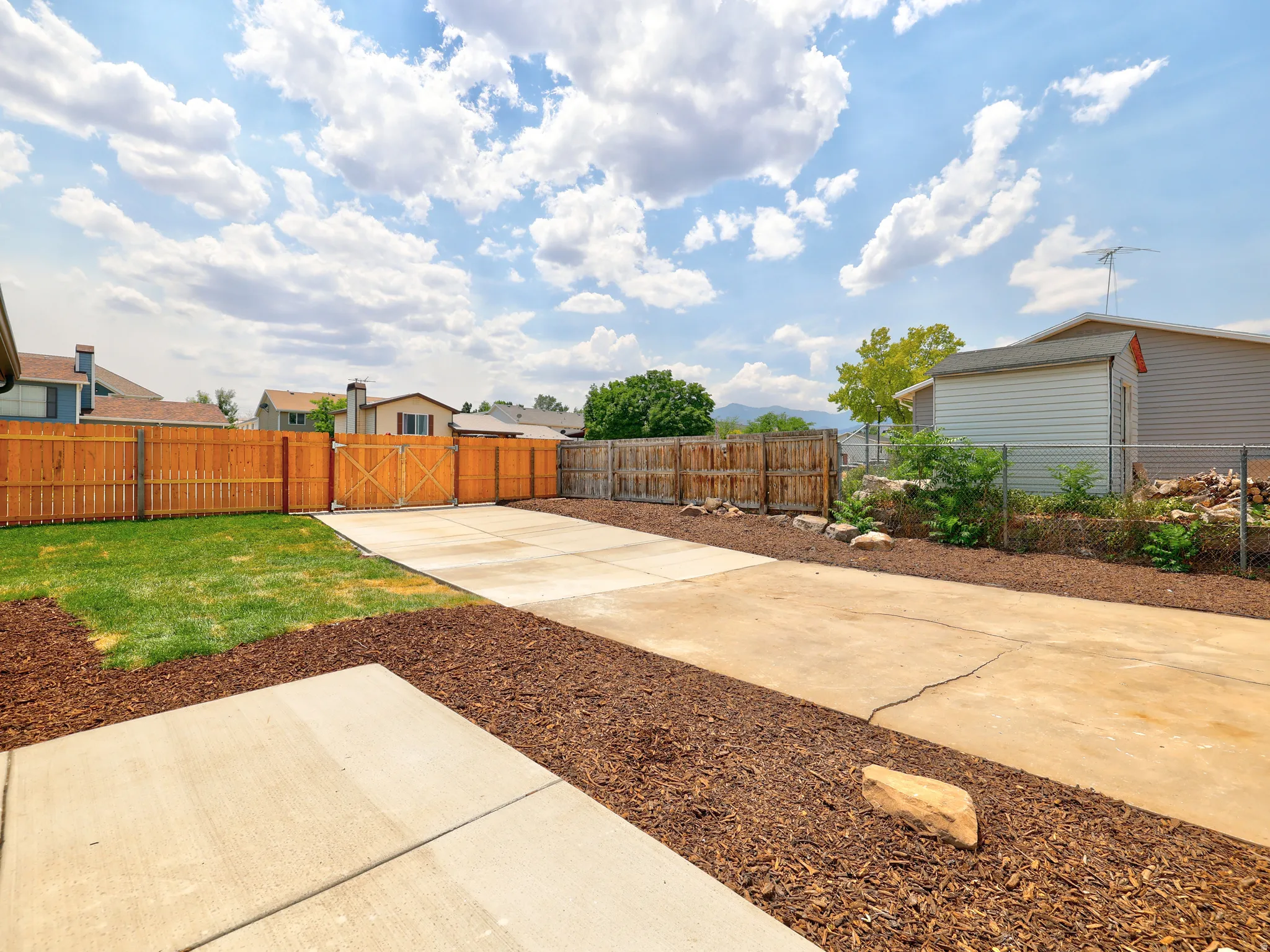 Expansive backyard featuring a combination of concrete patio, manicured lawn, and wood chip landscaping