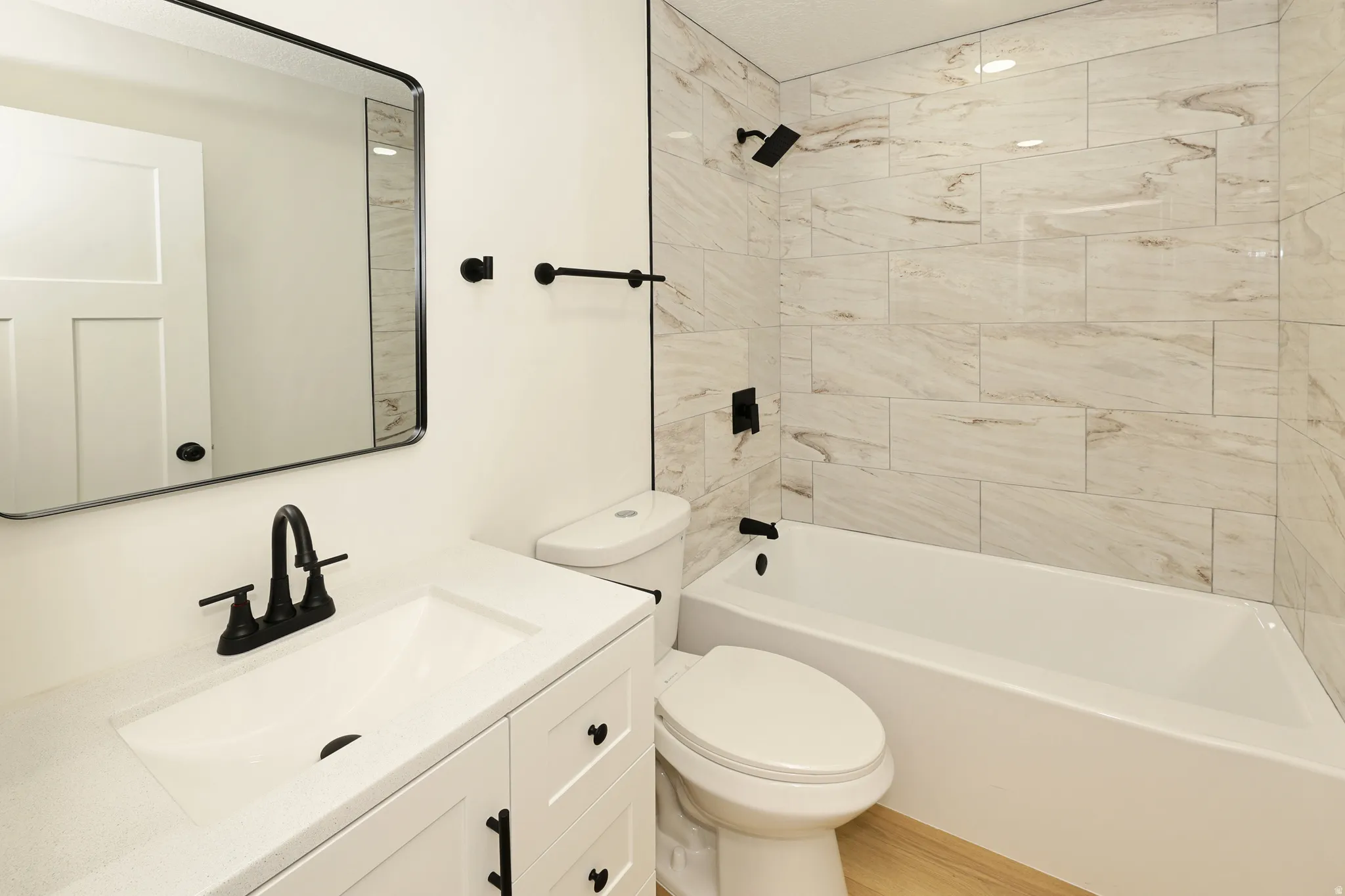 Bathroom featuring a white vanity with integrated sink, black hardware, a rectangular framed mirror, and a white bathtub with tile surround