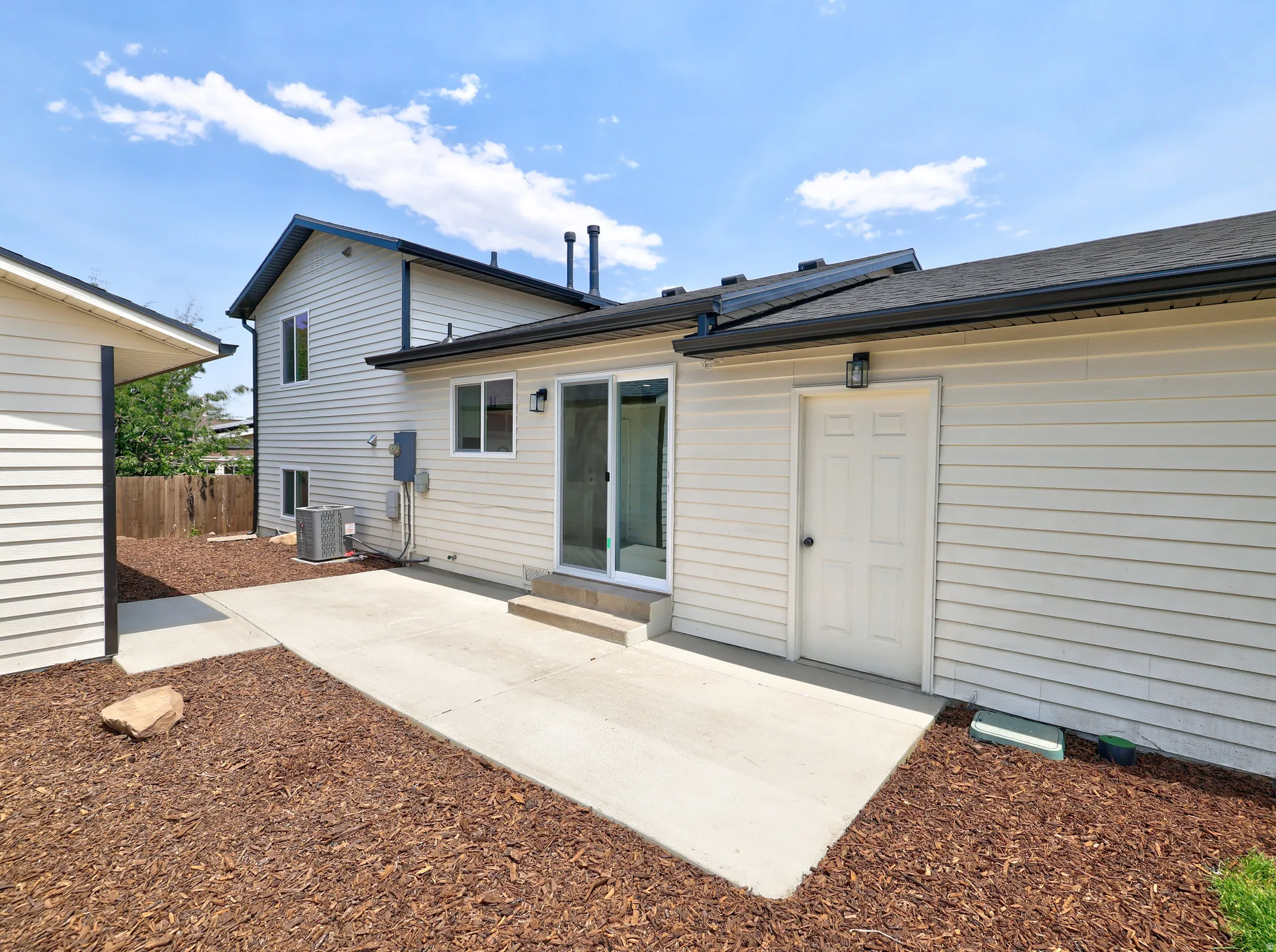 Outdoor patio area featuring concrete paving, dark brown mulch, and perimeter fencing