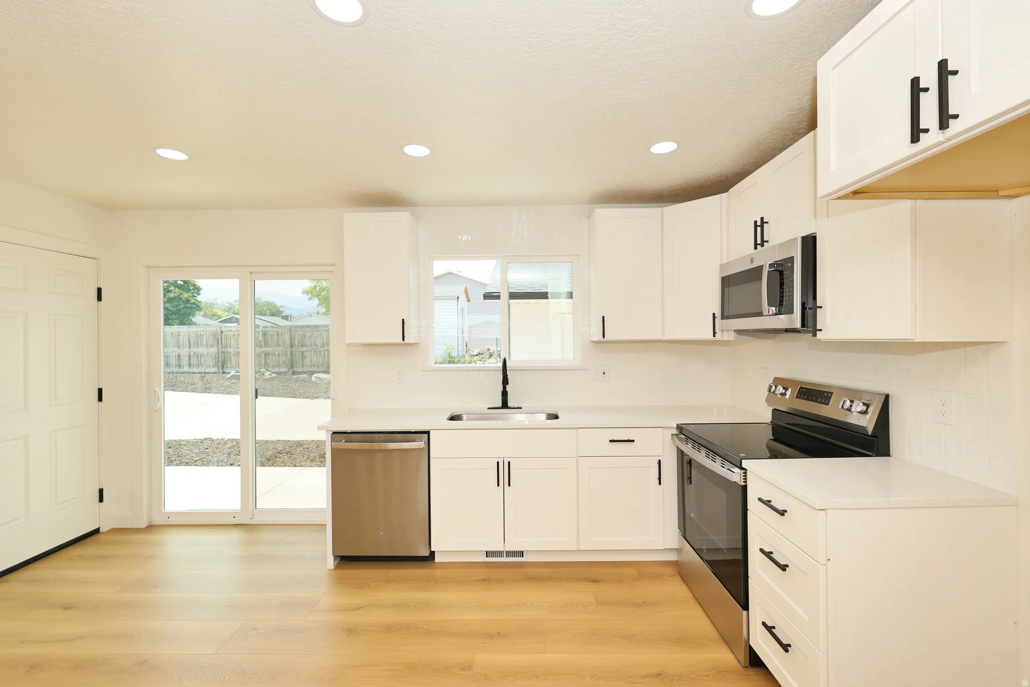 Kitchen featuring white shaker cabinetry, stainless steel appliances, light-colored countertops, wood-finish flooring, and recessed lighting