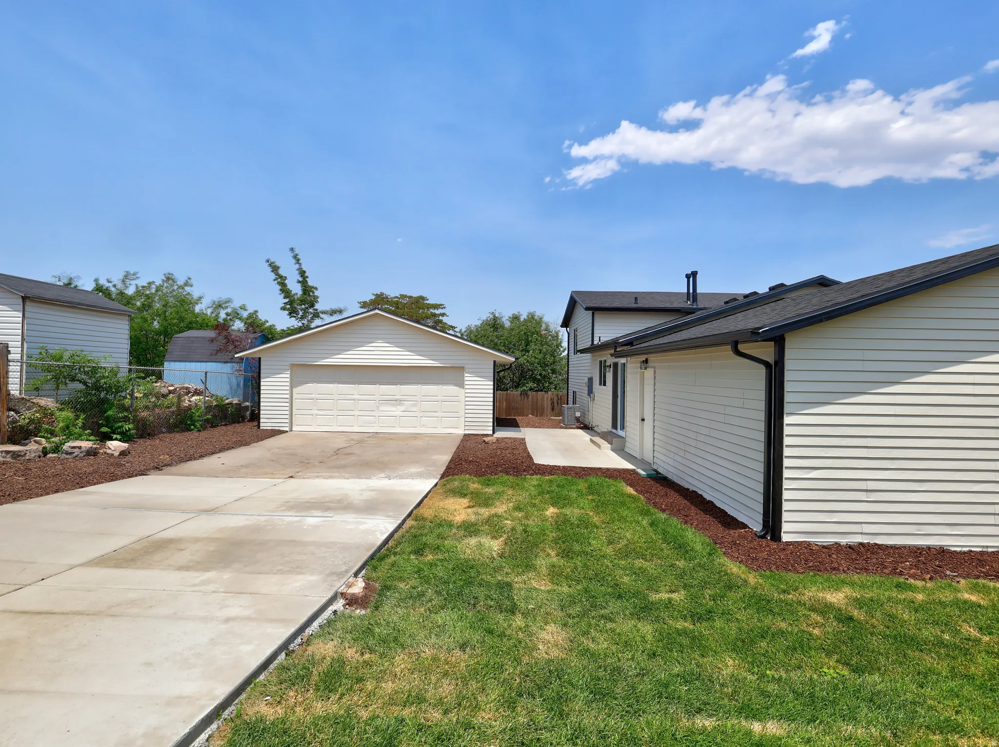Detached garage with a paneled door, a concrete driveway, and surrounding wood chip landscaping