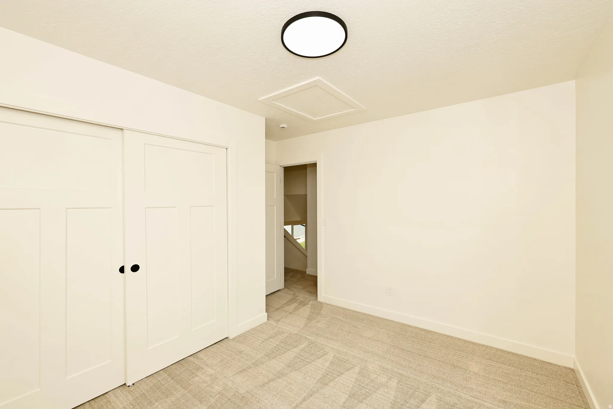 Room featuring light-toned carpeting, white walls, and a modern circular flush-mount ceiling light fixture