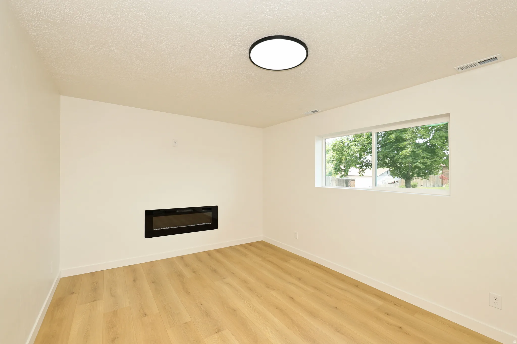 Room featuring a rectangular window, recessed electric fireplace, light wood-finish flooring, and a flush-mount ceiling light fixture