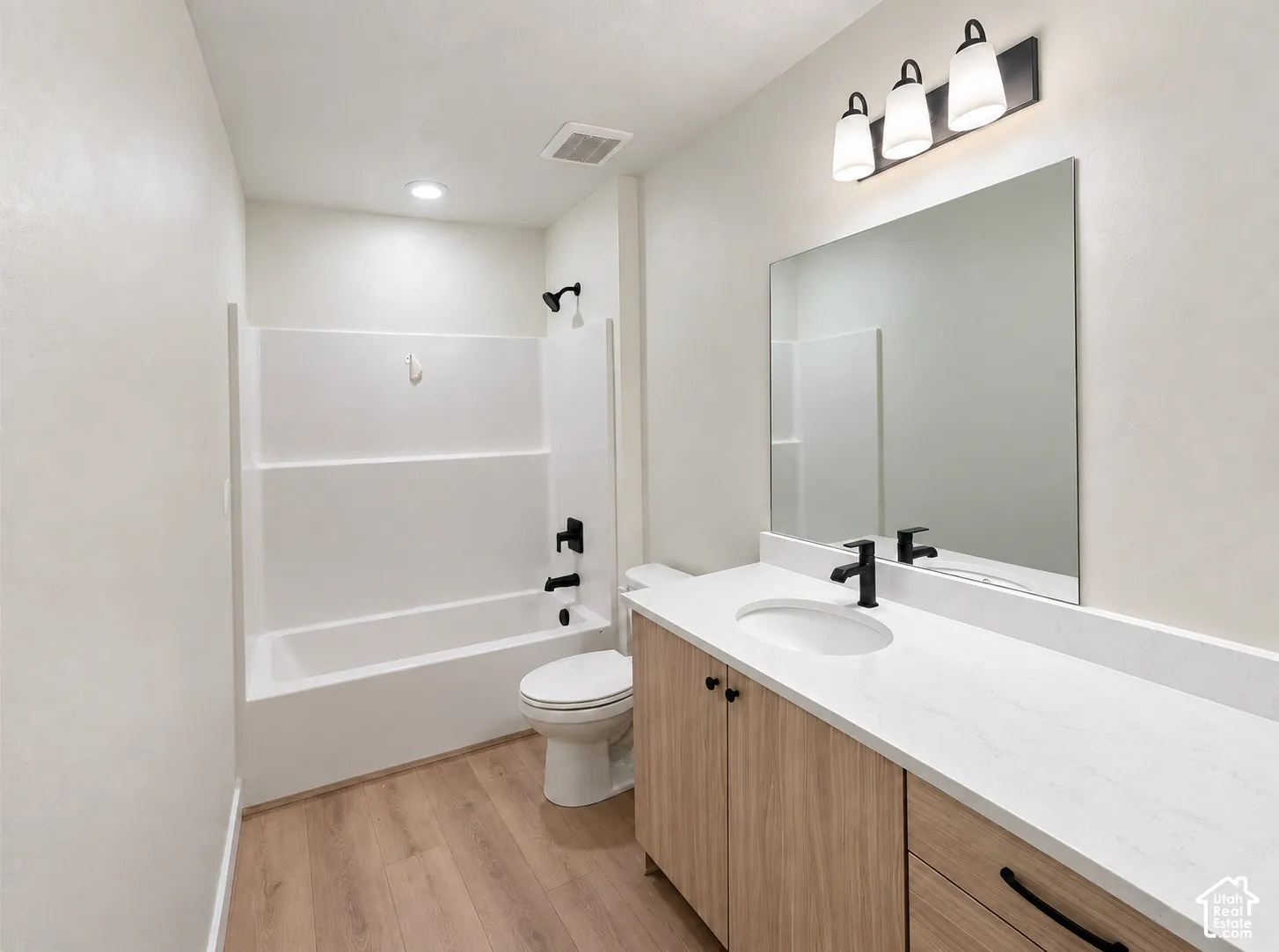 Bathroom featuring a white tub and shower surround, light wood-finish flooring, and a vanity with a white countertop
