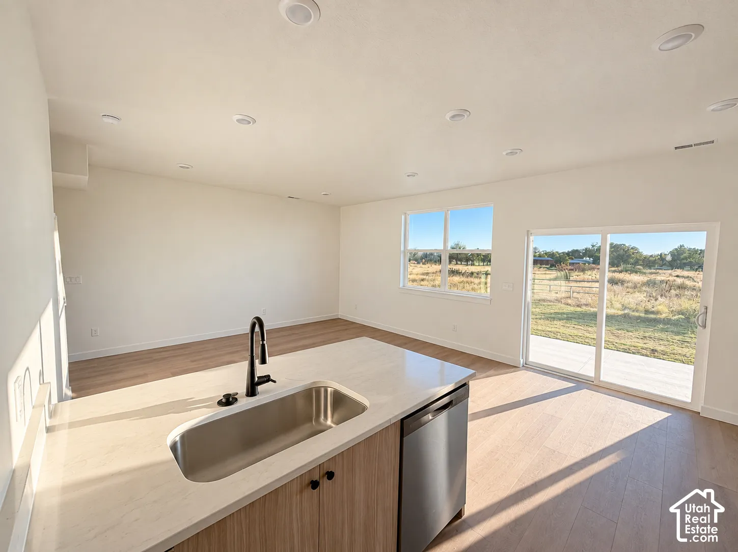 Kitchen island with a stainless steel sink and matte black faucet, integrated dishwasher, and light-toned wood-finish cabinetry