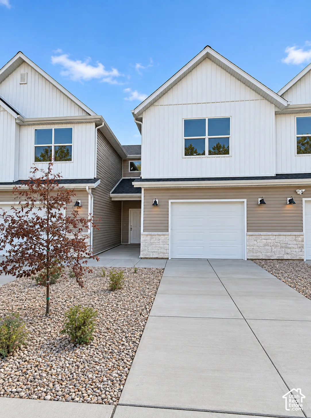 Contemporary townhome featuring a two-tone facade, attached garage, stone accents, and a concrete driveway