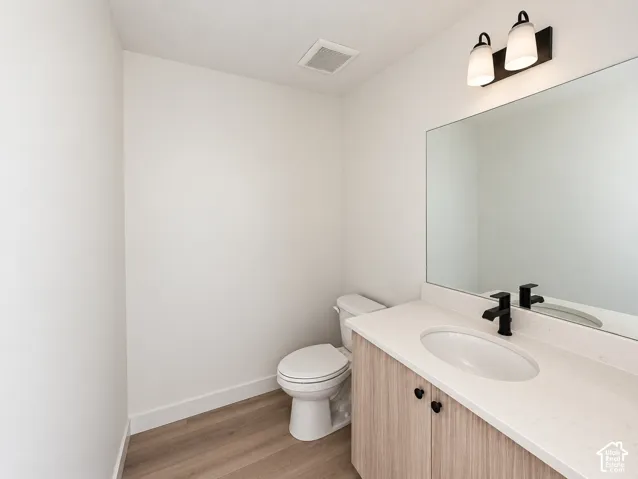 Wood-finish flooring, light wood-look vanity with black hardware, white countertop, black faucet, and rectangular mirror