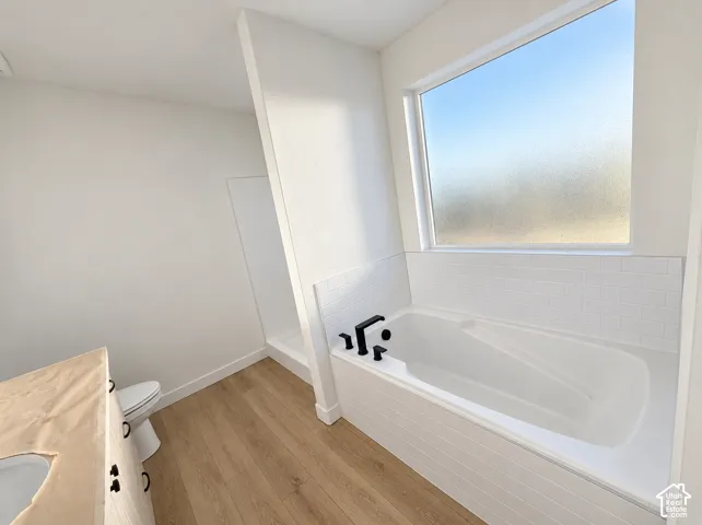 Soaking tub with subway tile surround, wood-finish flooring, and a privacy window