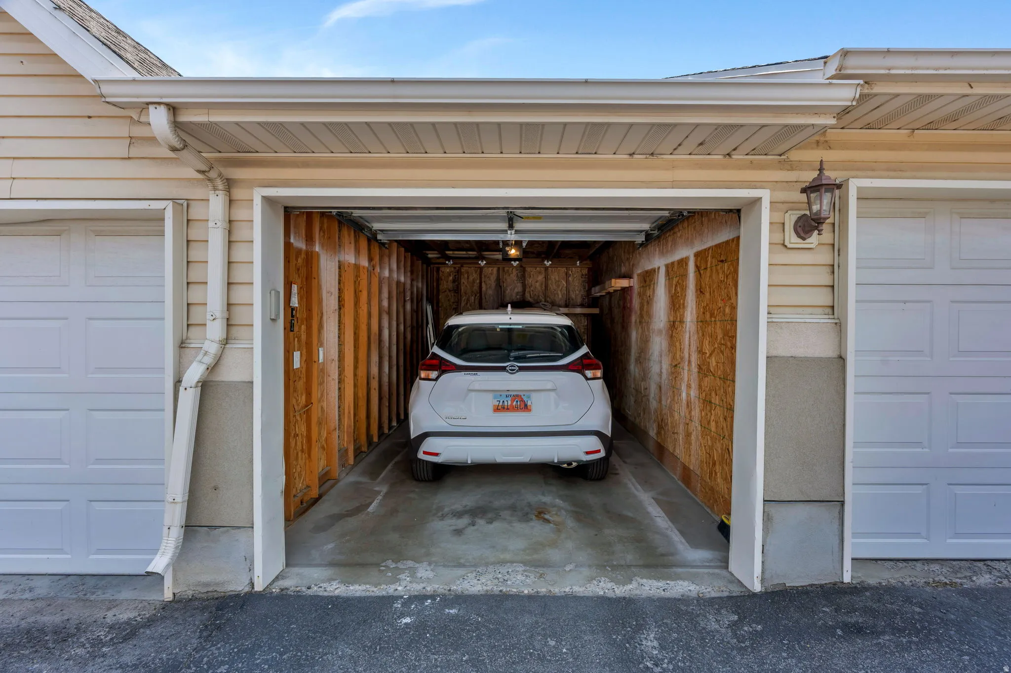 Attached garage with a white panel door, concrete flooring, and interior wood-finish walls