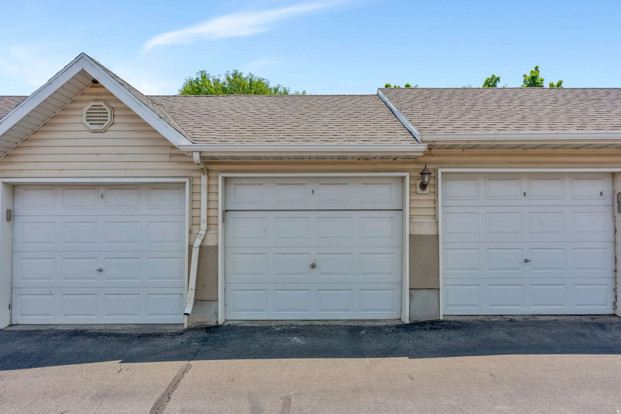 Exterior featuring three white paneled garage doors, light-colored siding, a gable roofline with an octagonal vent, and a shingle roof