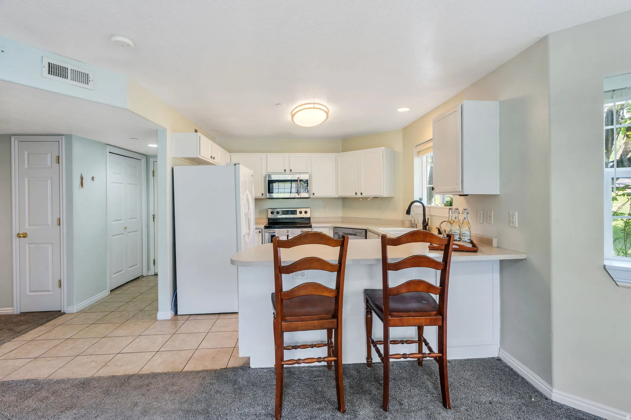 Bright kitchen featuring white cabinetry, light countertops, stainless steel appliances, and a breakfast bar
