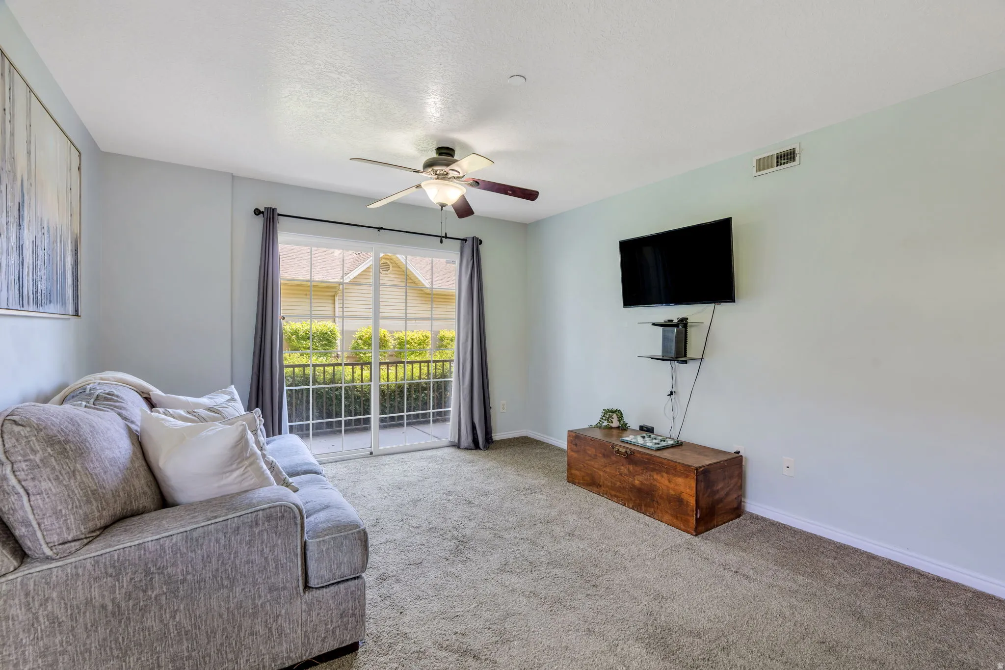 Carpeted living area featuring a ceiling fan with light fixture, sliding glass door to exterior, and wall-mounted shelving