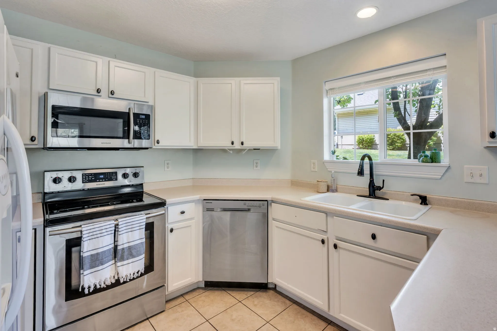 Kitchen featuring white cabinetry, stainless steel appliances, a double basin sink with a gooseneck faucet, light-toned countertops, and tile flooring