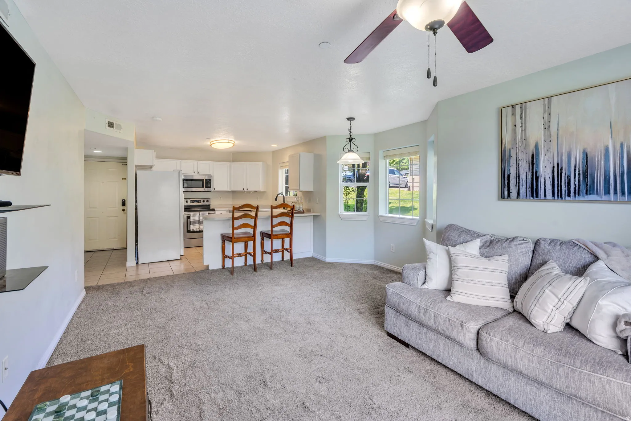 Open-concept living area featuring light-colored carpeting, a ceiling fan, and bay windows