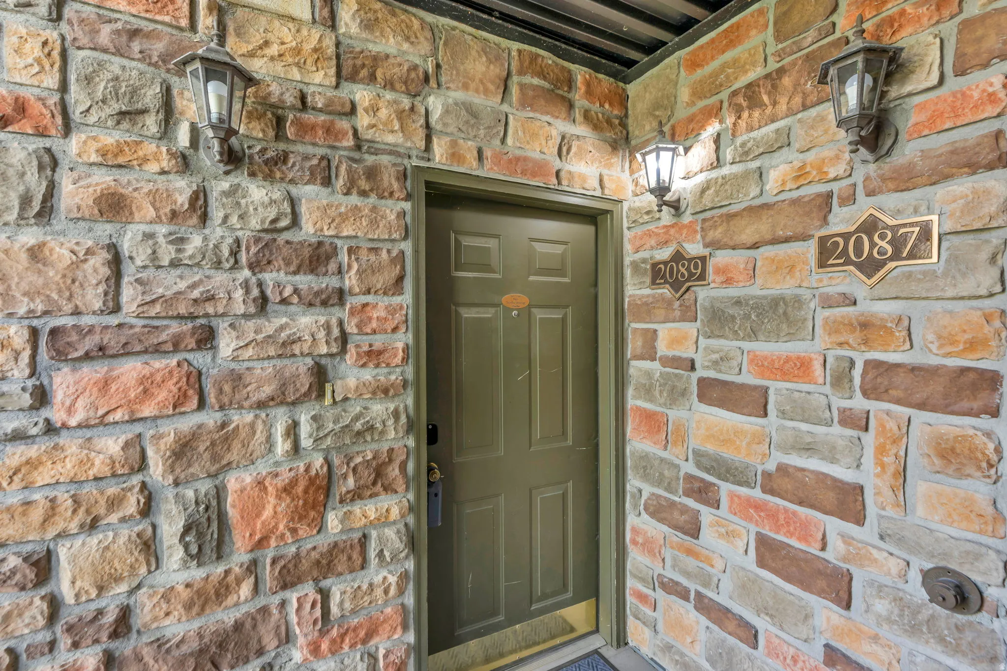 Entryway featuring a paneled door with a brass kick plate, flanked by stone veneer walls with varied earth tones