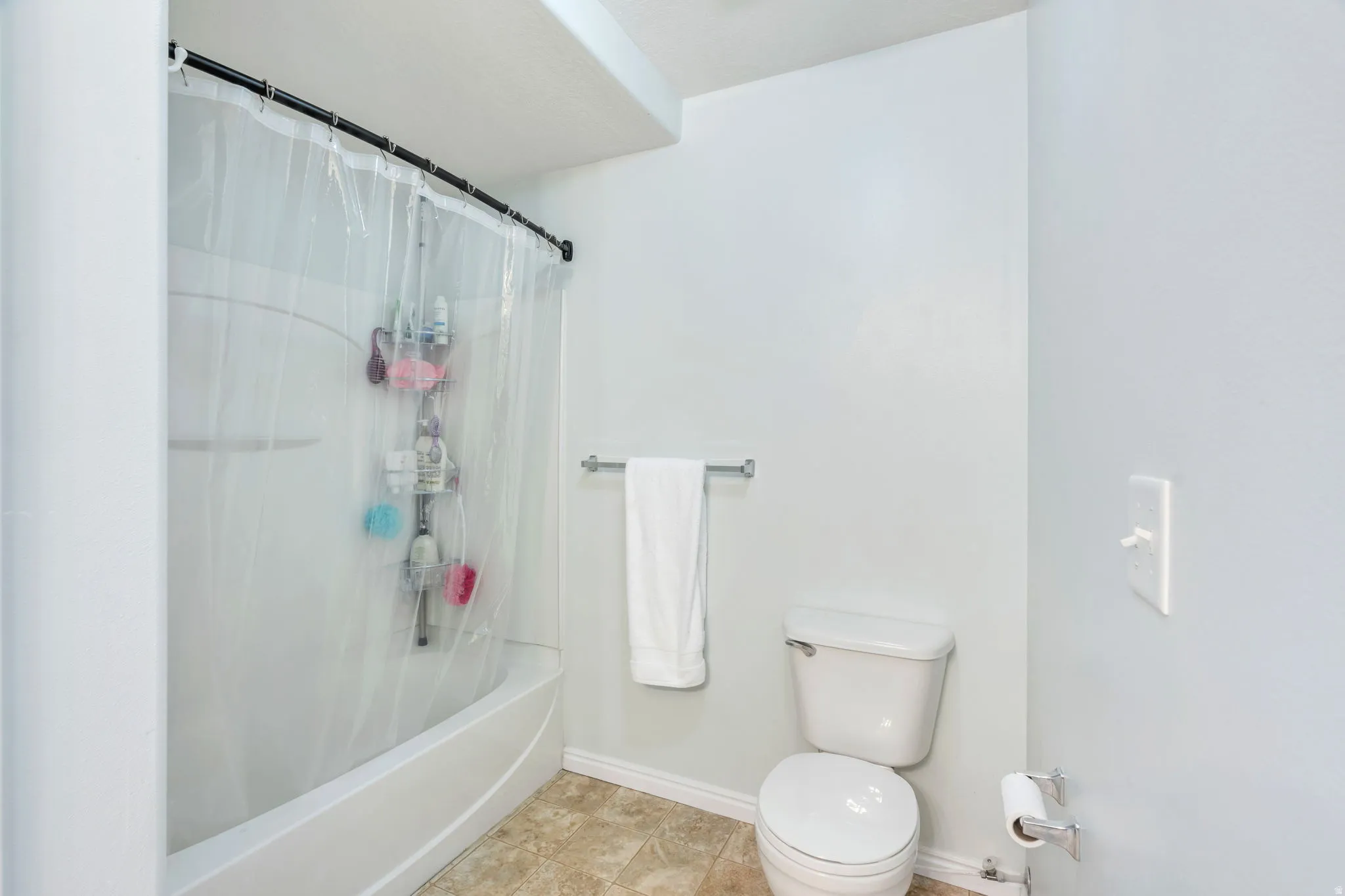 Bathroom featuring a shower/tub combination with a curved shower rod, a white toilet, and neutral-toned wall paint