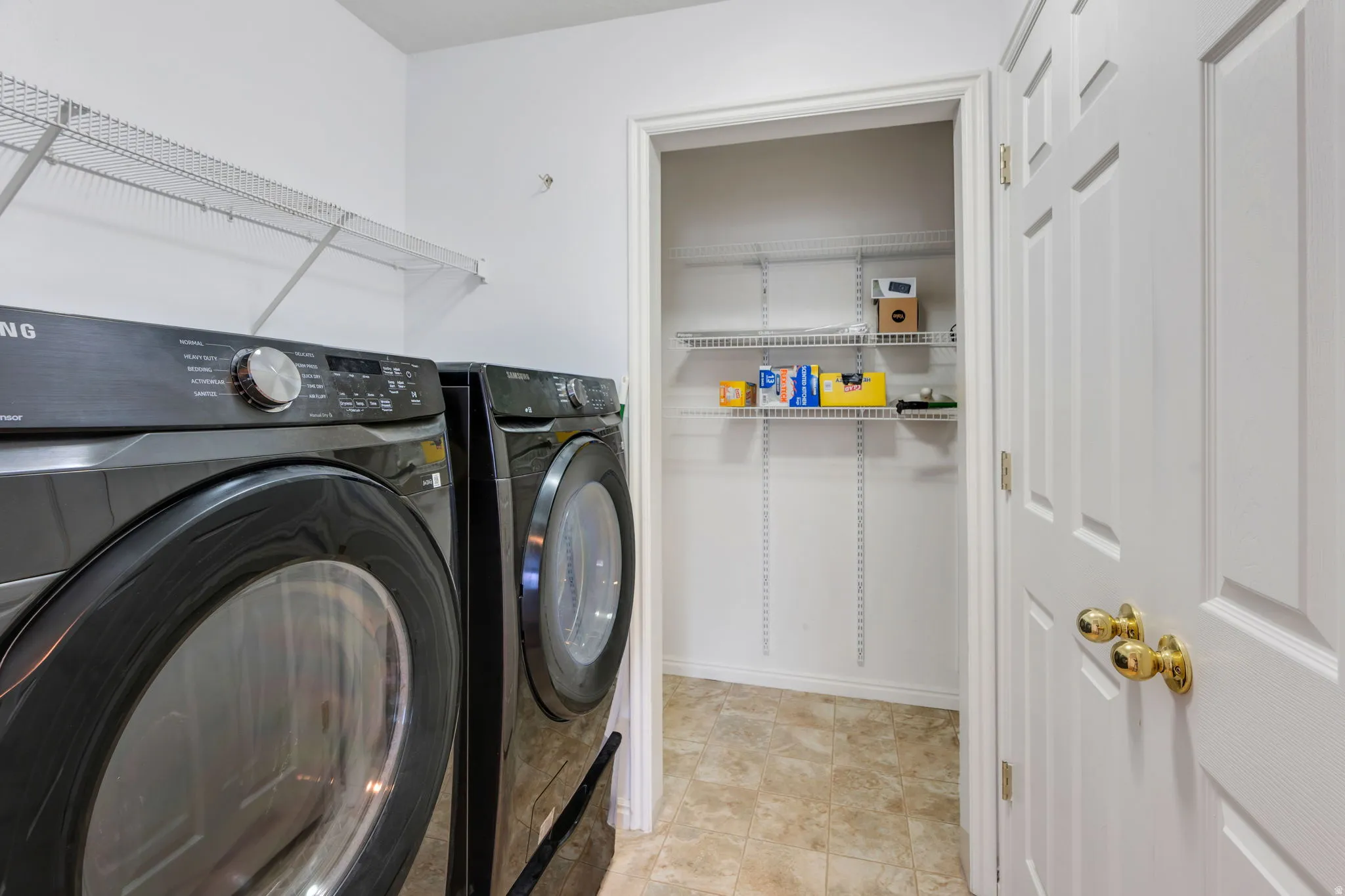 Dedicated laundry space featuring a side-by-side washer and dryer, wire shelving, and a paneled door with brass hardware