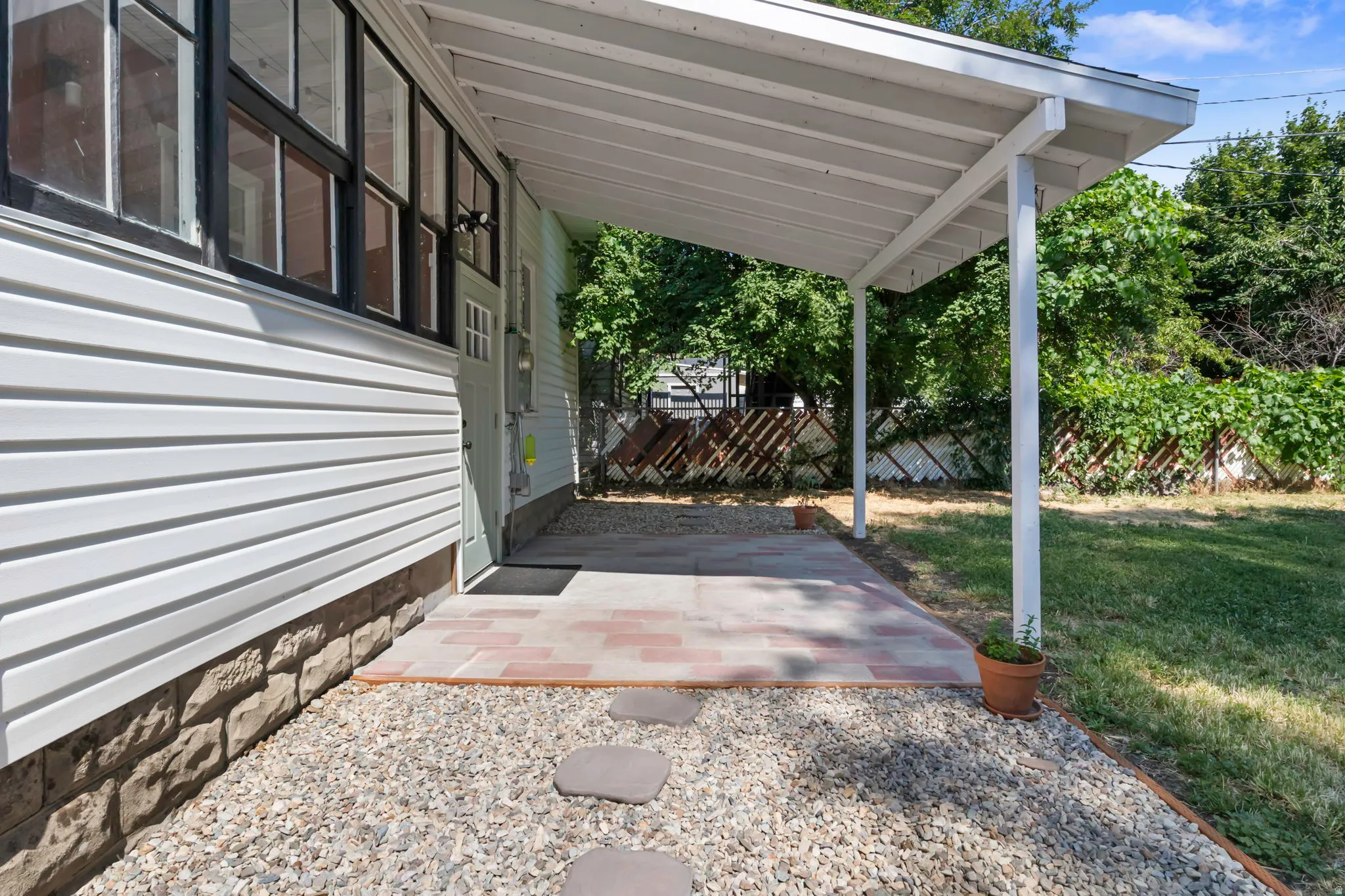 Covered patio with brick paver flooring and gravel landscaping, featuring a white vinyl siding exterior with a stone veneer foundation