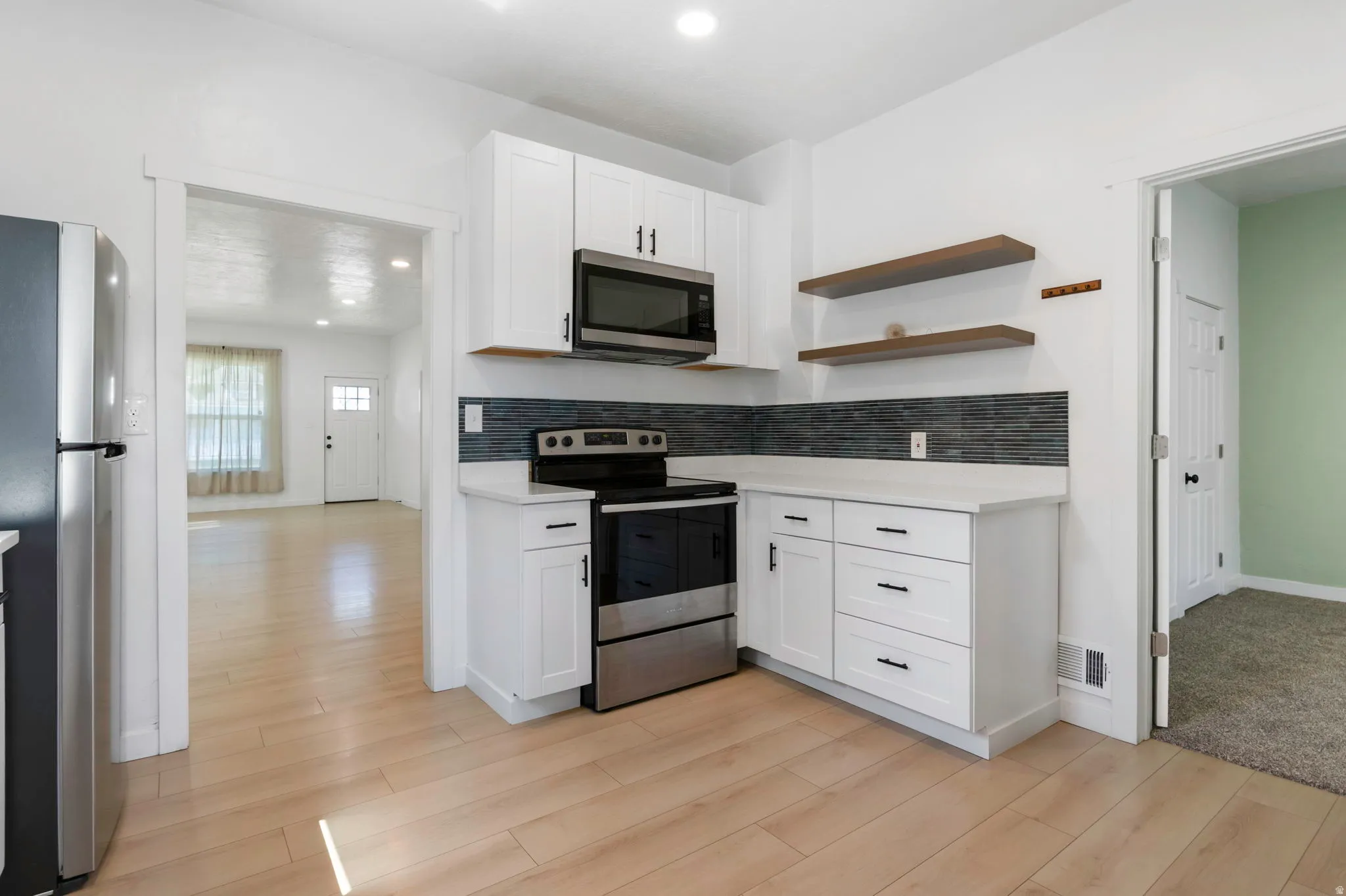 Kitchen featuring white cabinetry, stainless steel appliances, dark gray tile backsplash, light wood-finish flooring, and open shelving