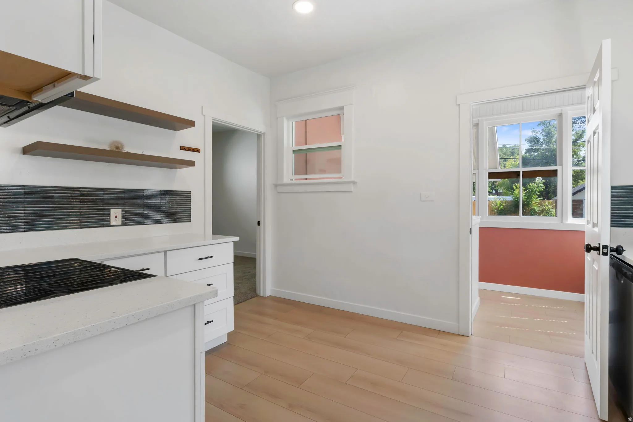 Bright kitchen featuring wood-finish flooring, white cabinetry, integrated cooktop, stone countertops, and open shelving