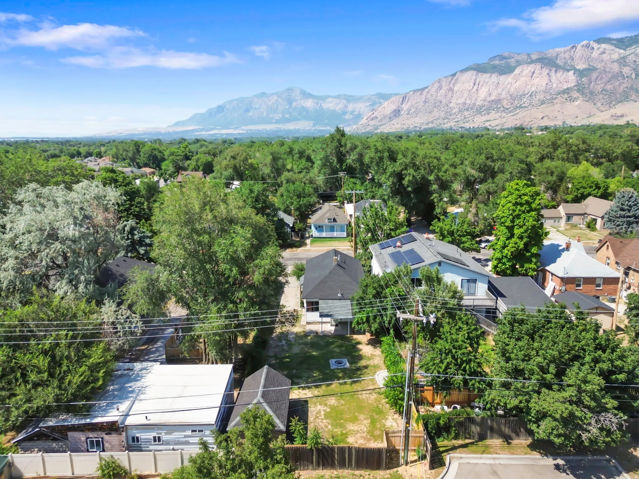 Property featuring a light-colored exterior with dark roof, multiple mature trees, and a mountain backdrop